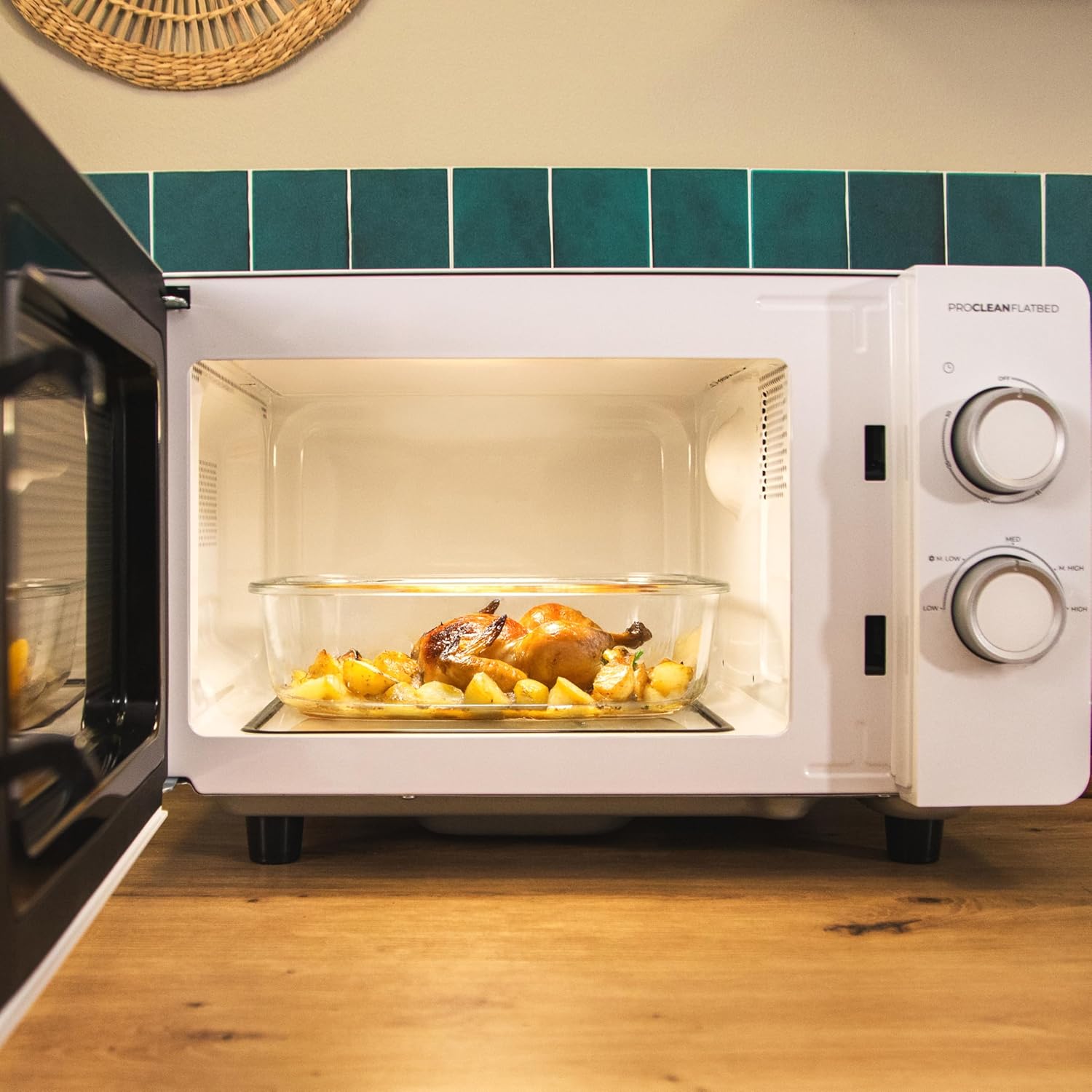 Inside the microwave, a glass dish with a roasted chicken and potatoes is placed on the flat ceramic base