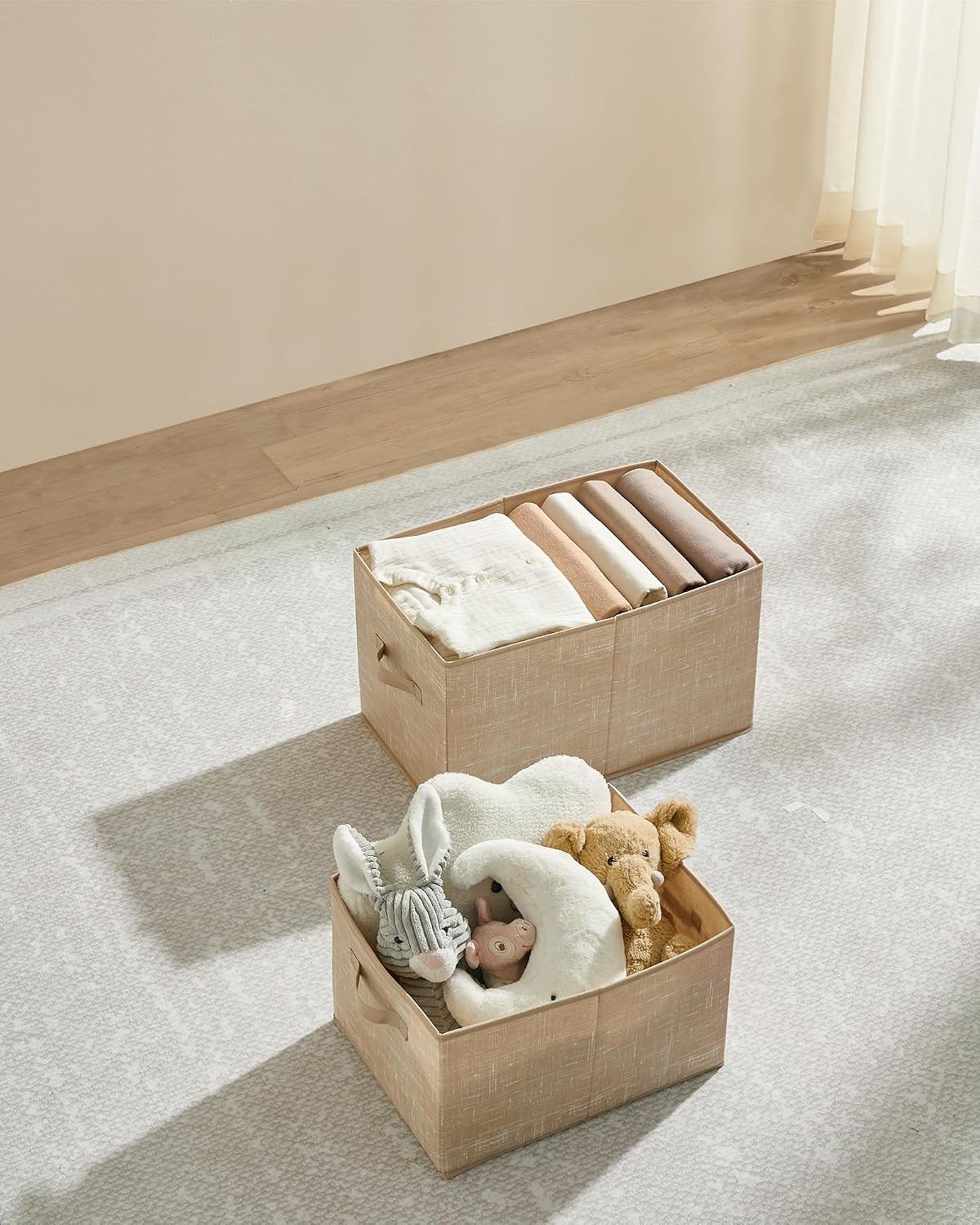 Two sand beige SONGMICS storage boxes on a light-colored rug, one filled with folded blankets and the other with children's toys.