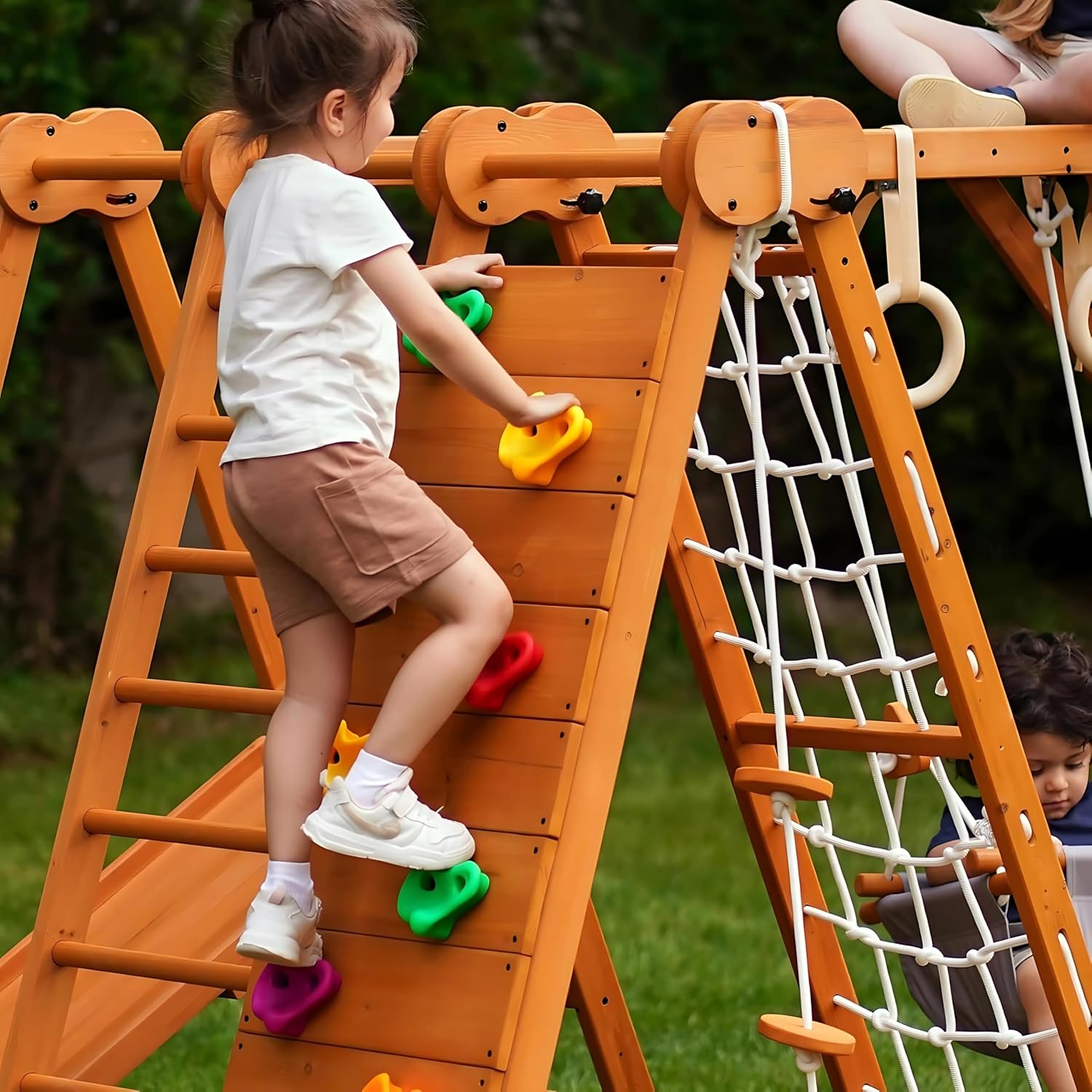 A child actively climbing the colorful holds of the rock climbing wall on the Avenlur 8-in-1 Playset, demonstrating its use.