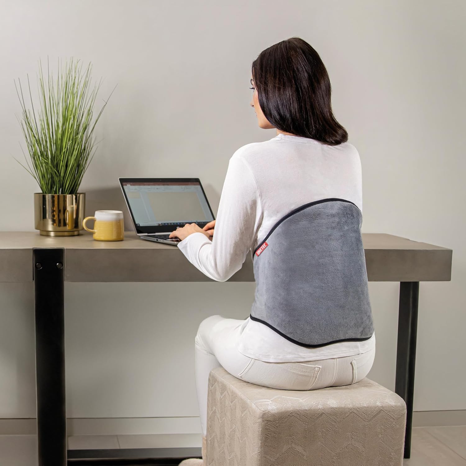 Woman using Imetec Intellisense Lumbar Heating Pad at a desk