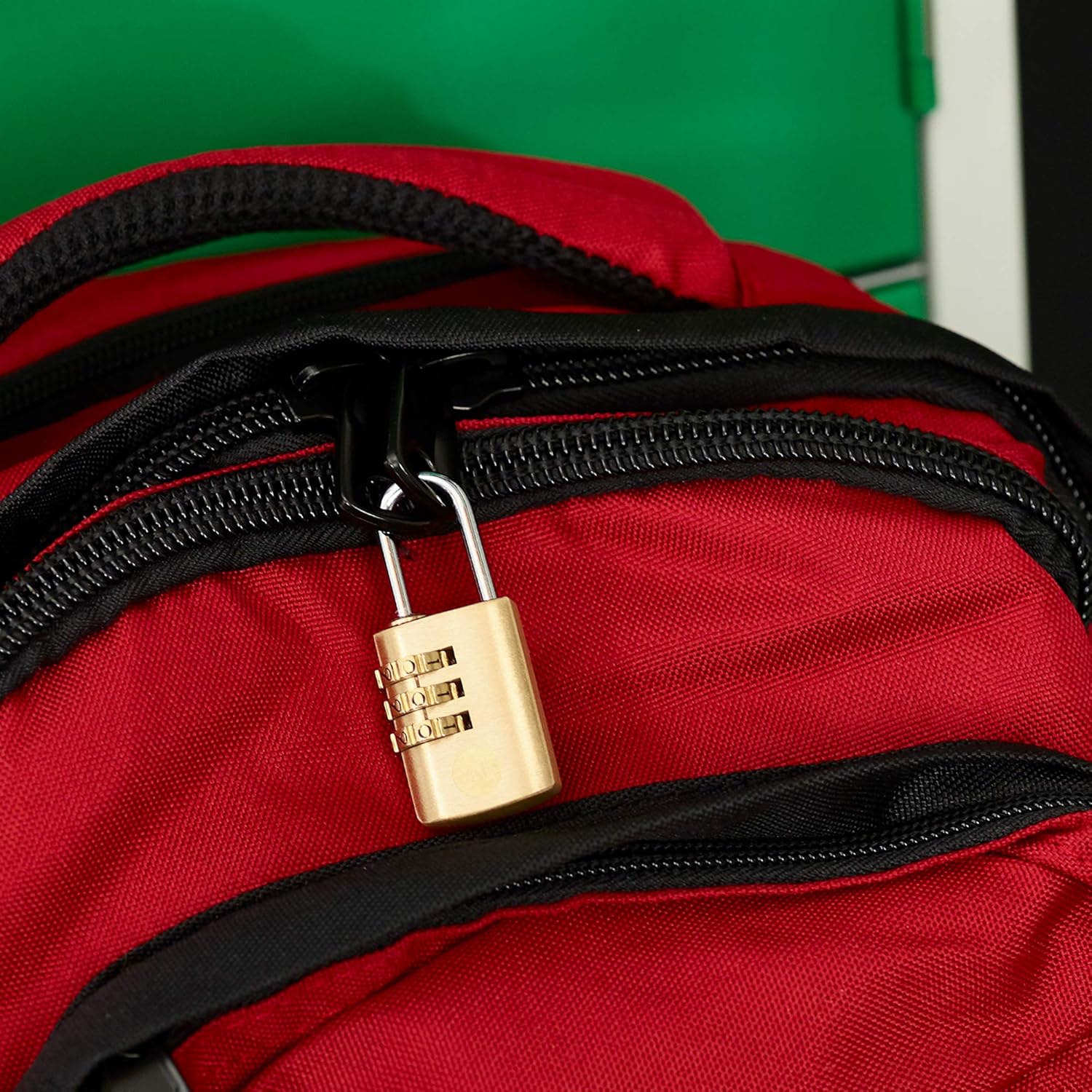 A Yale combination padlock securing the zipper of a red backpack.