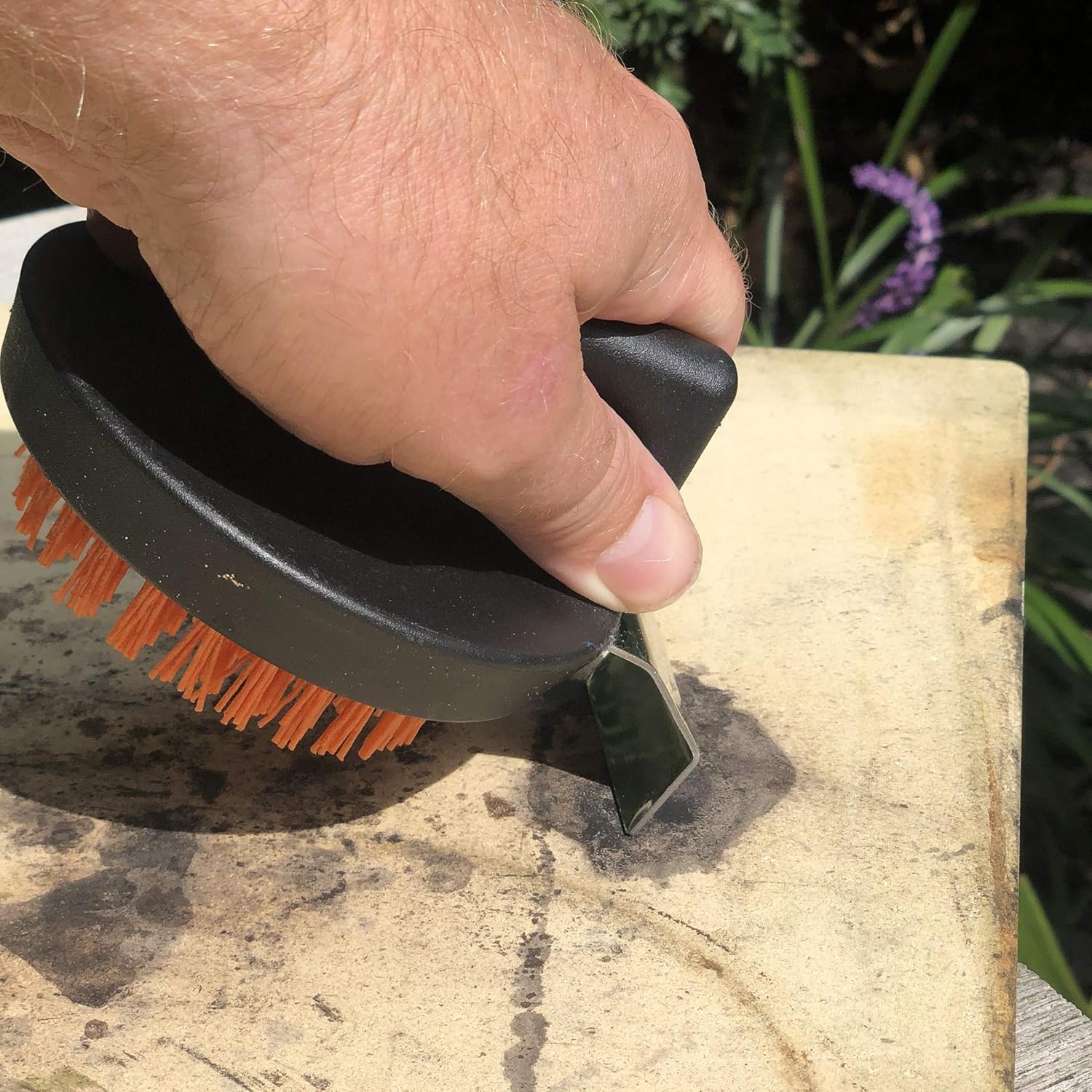 Hand using the Outset cleaning brush with its scraper on a pizza stone to remove residue