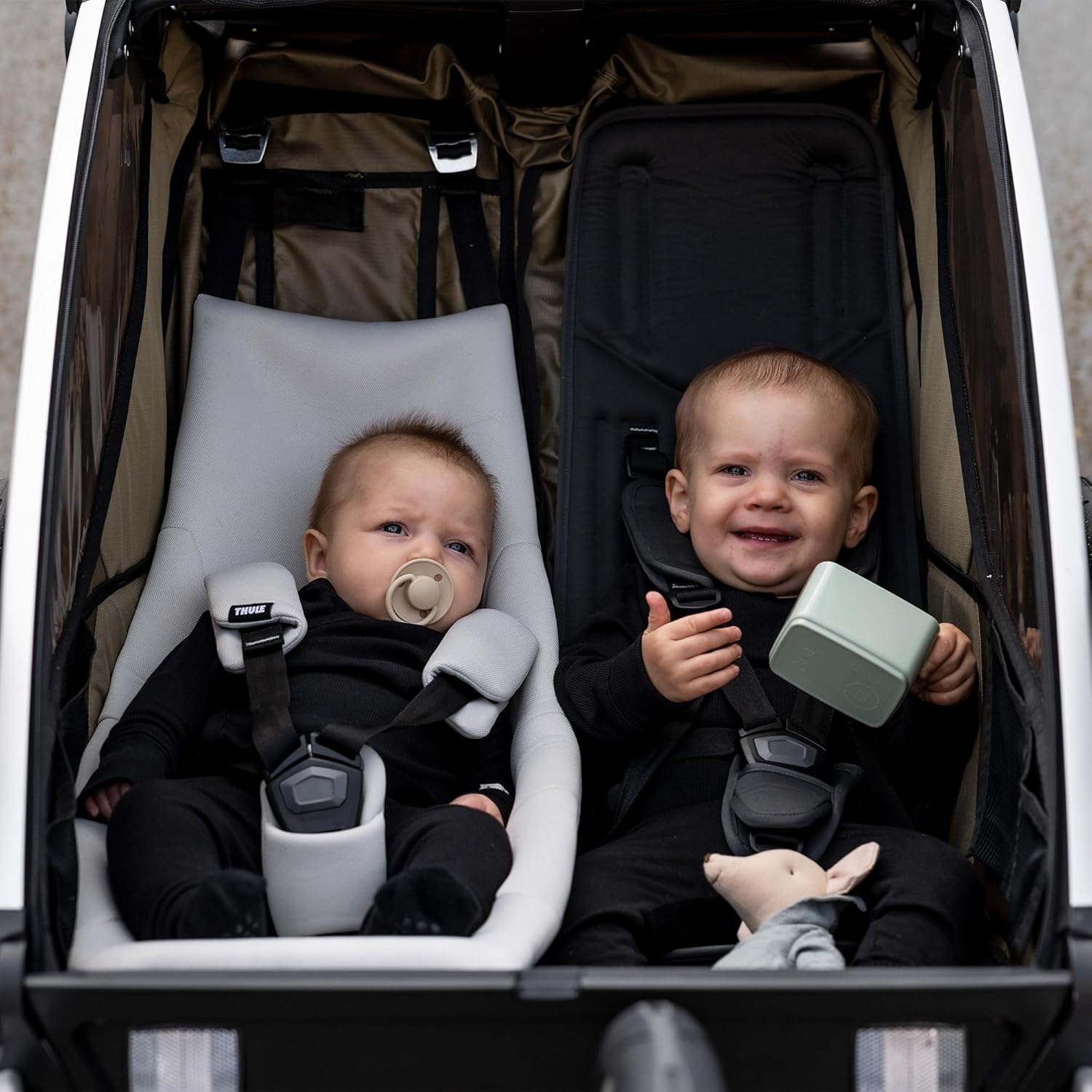 Two infants in a double Thule Chariot, one in the infant sling.