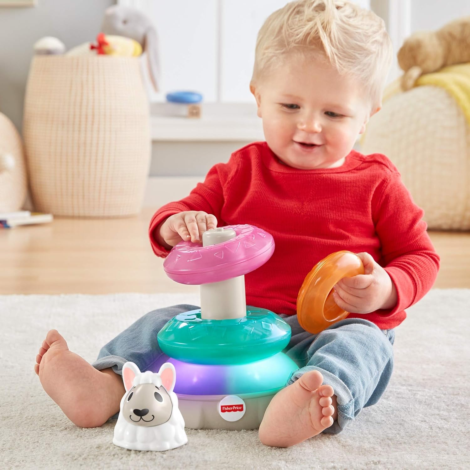 A baby sitting on a rug, happily playing with the Fisher-Price Linkimals Llama Stacker, holding one of the colorful rings.