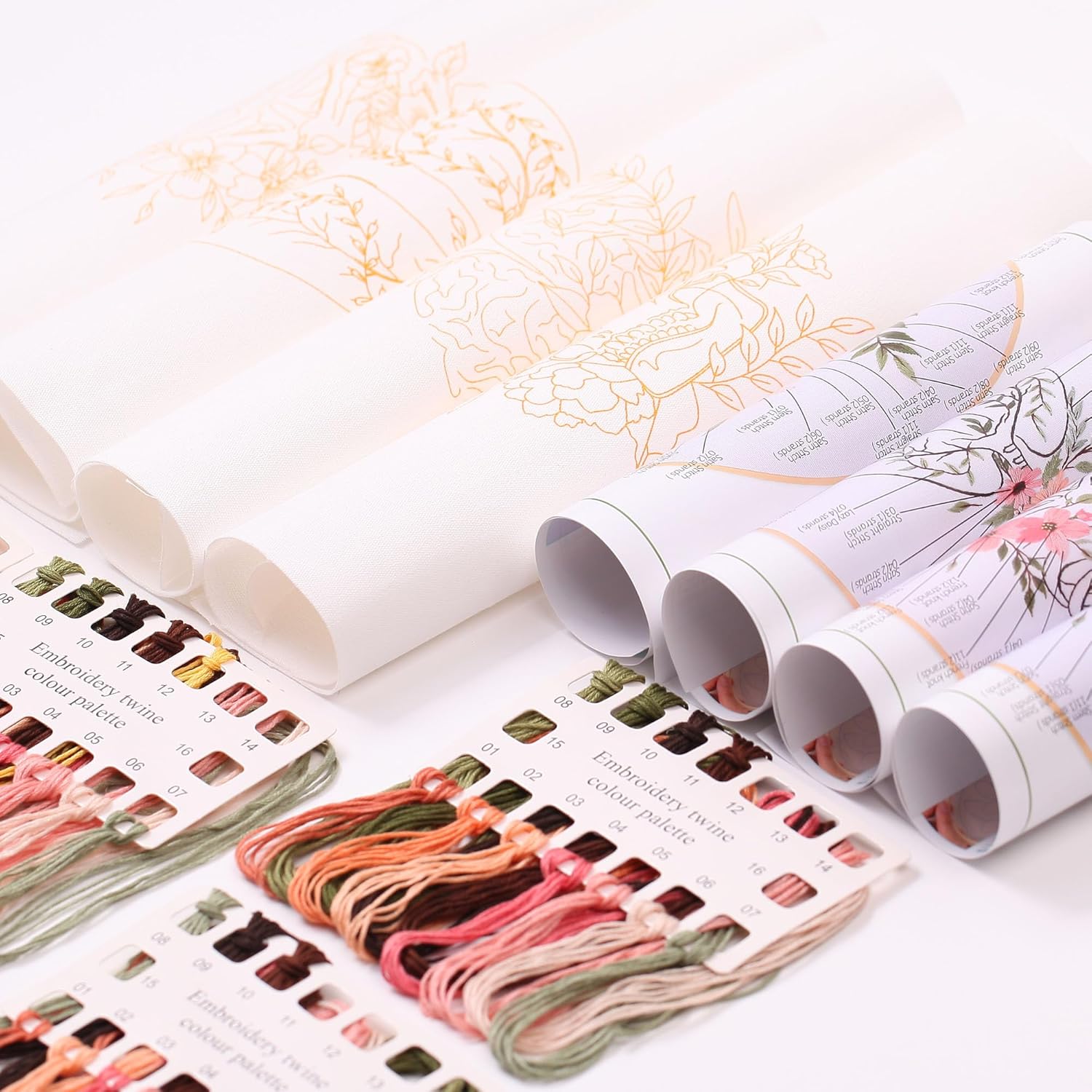 Close-up of embroidery materials including rolled fabric patterns, thread palette, and instruction sheets.