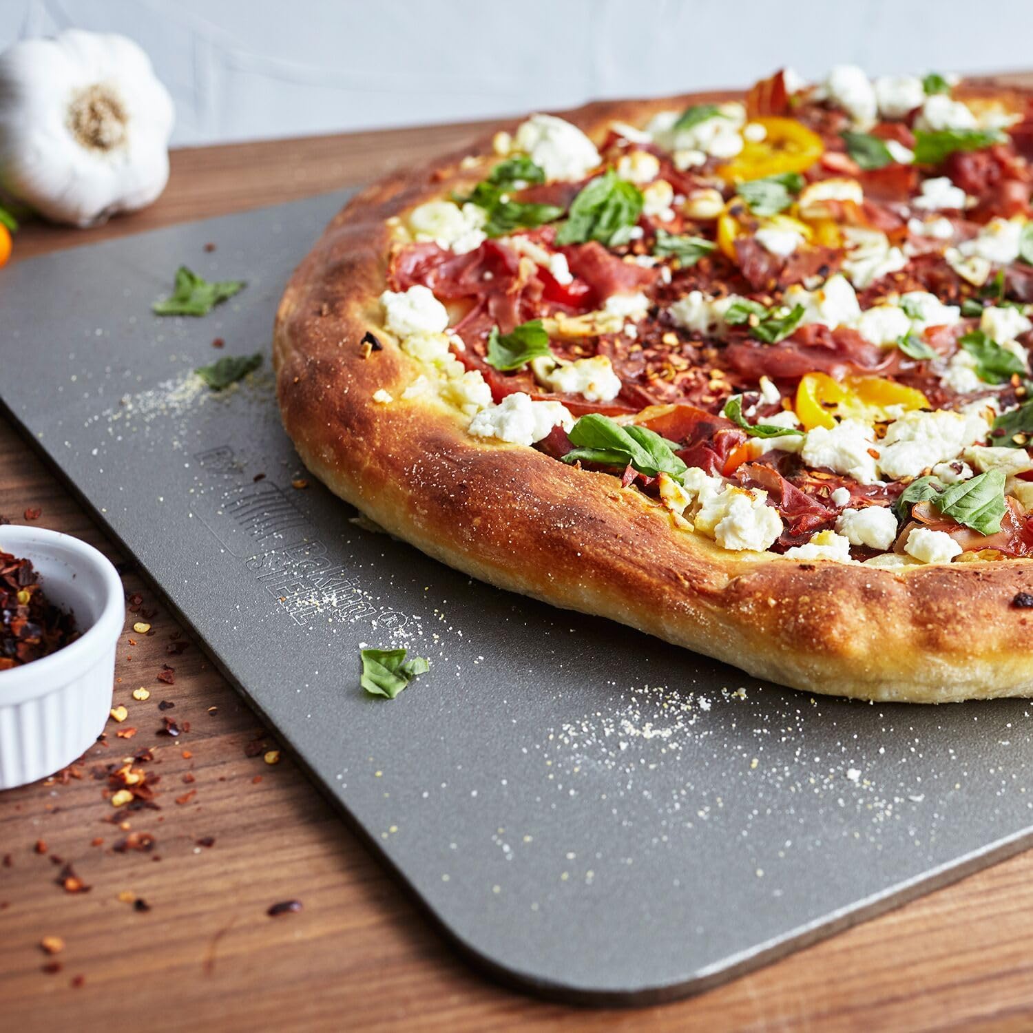 A gourmet pizza with prosciutto, ricotta, and basil on the Sur La Table Baking Steel.