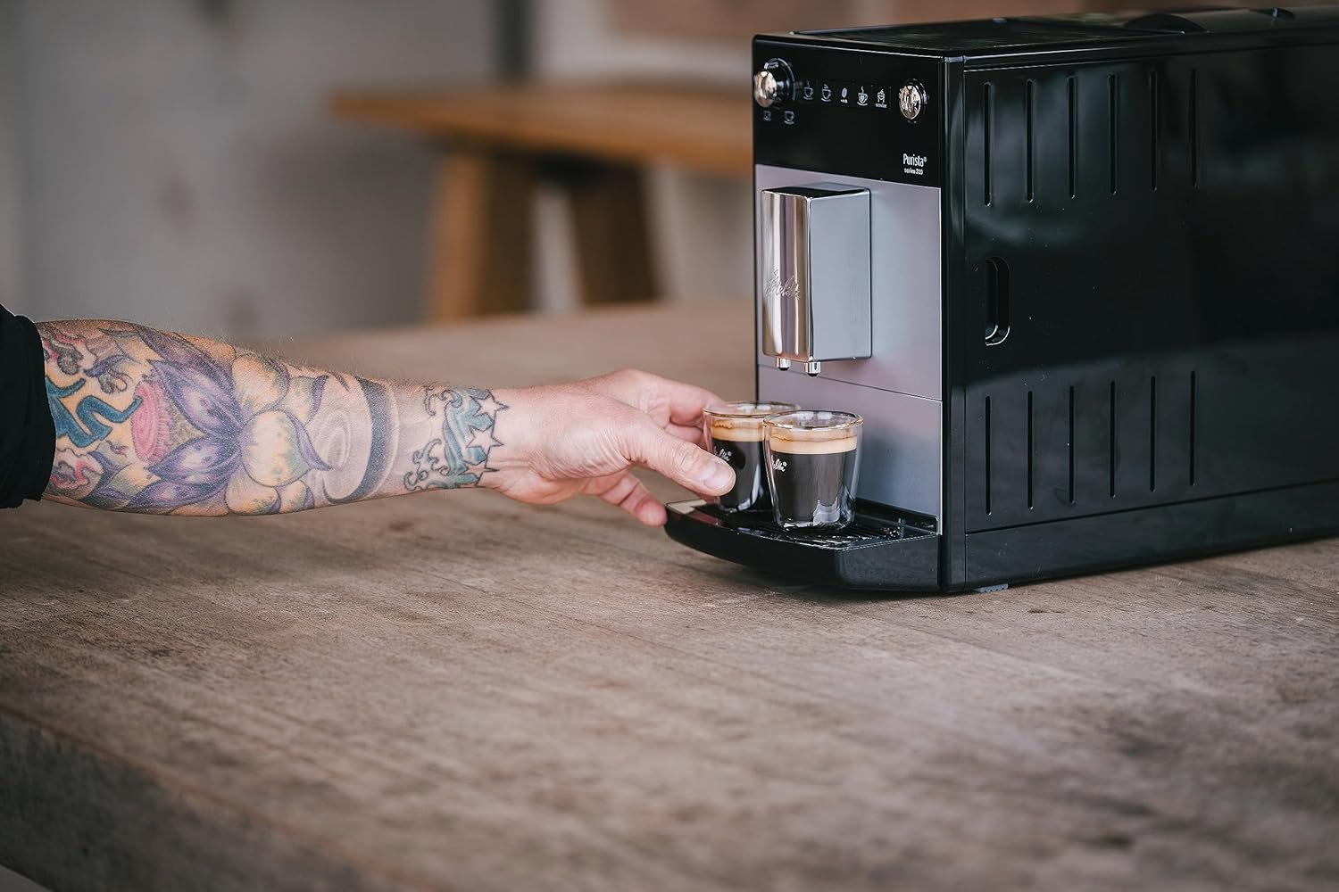 Hand placing cups under the coffee spout of Melitta Purista