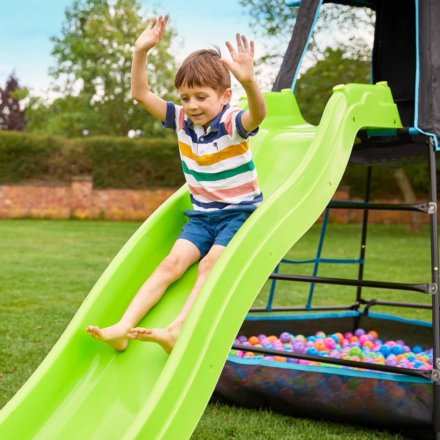 Child sliding down the green slide into a ball pit