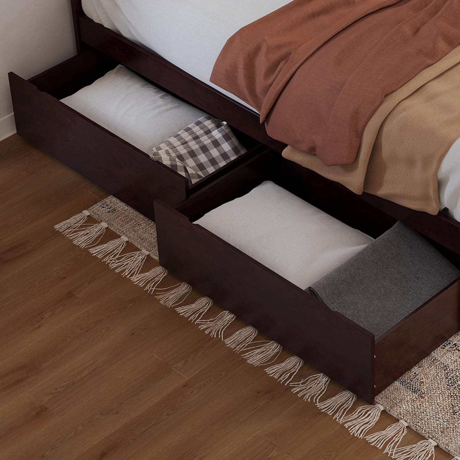 Two espresso under-bed drawers partially pulled out from under a bed, filled with pillows and blankets, on a wooden floor with a rug.
