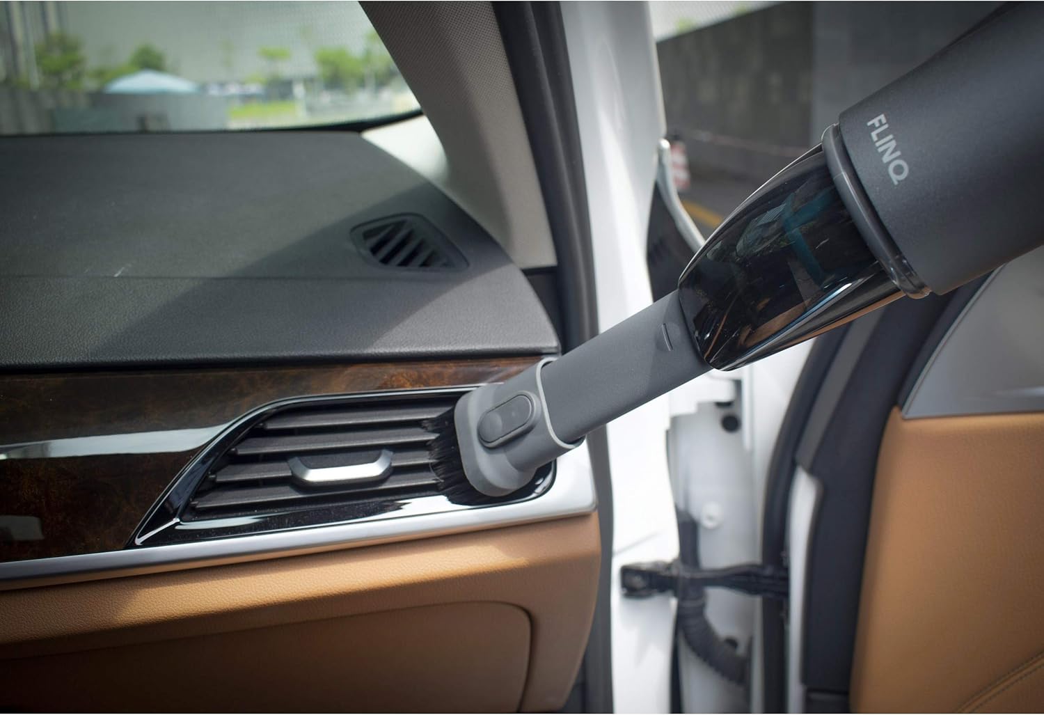 FLINQ handheld vacuum cleaner being used to clean a car interior vent with the brush attachment.