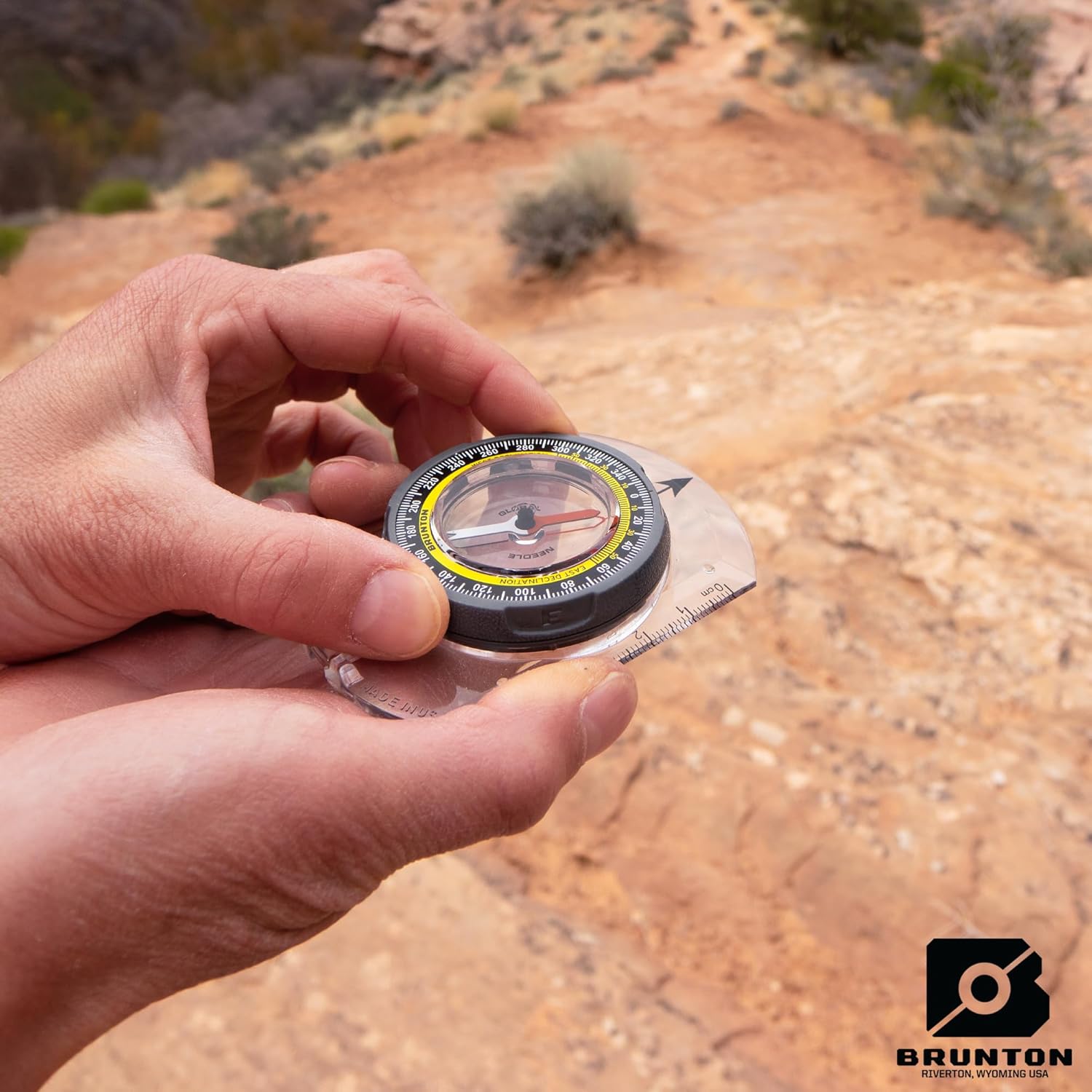 Close-up of hands adjusting the declination on a Brunton TruArc 3 compass by rotating the outer dial.