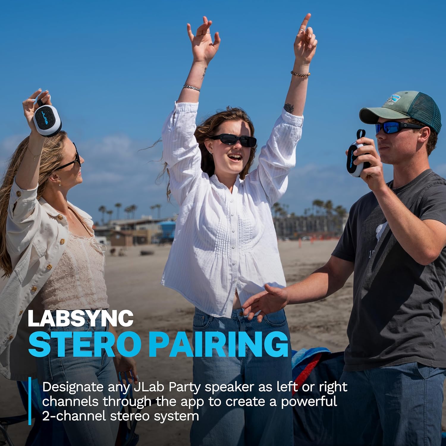 Пляжда үч адам, экөө JLab Pop Party динамиктерин кармап, стерео жупташтыруу функциясын көрсөтүп жатышат.