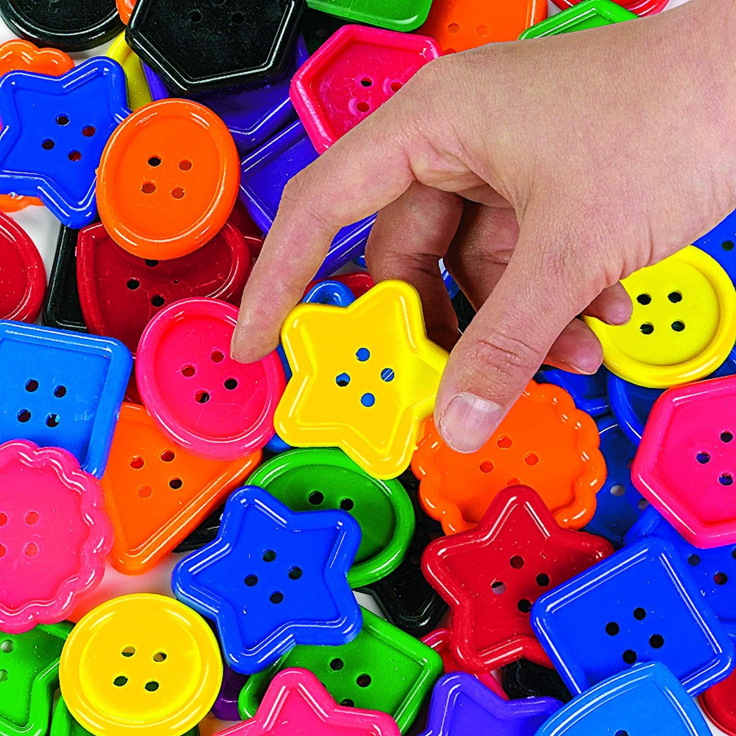 A hand reaching for a yellow star-shaped button from a colorful pile, demonstrating sorting.