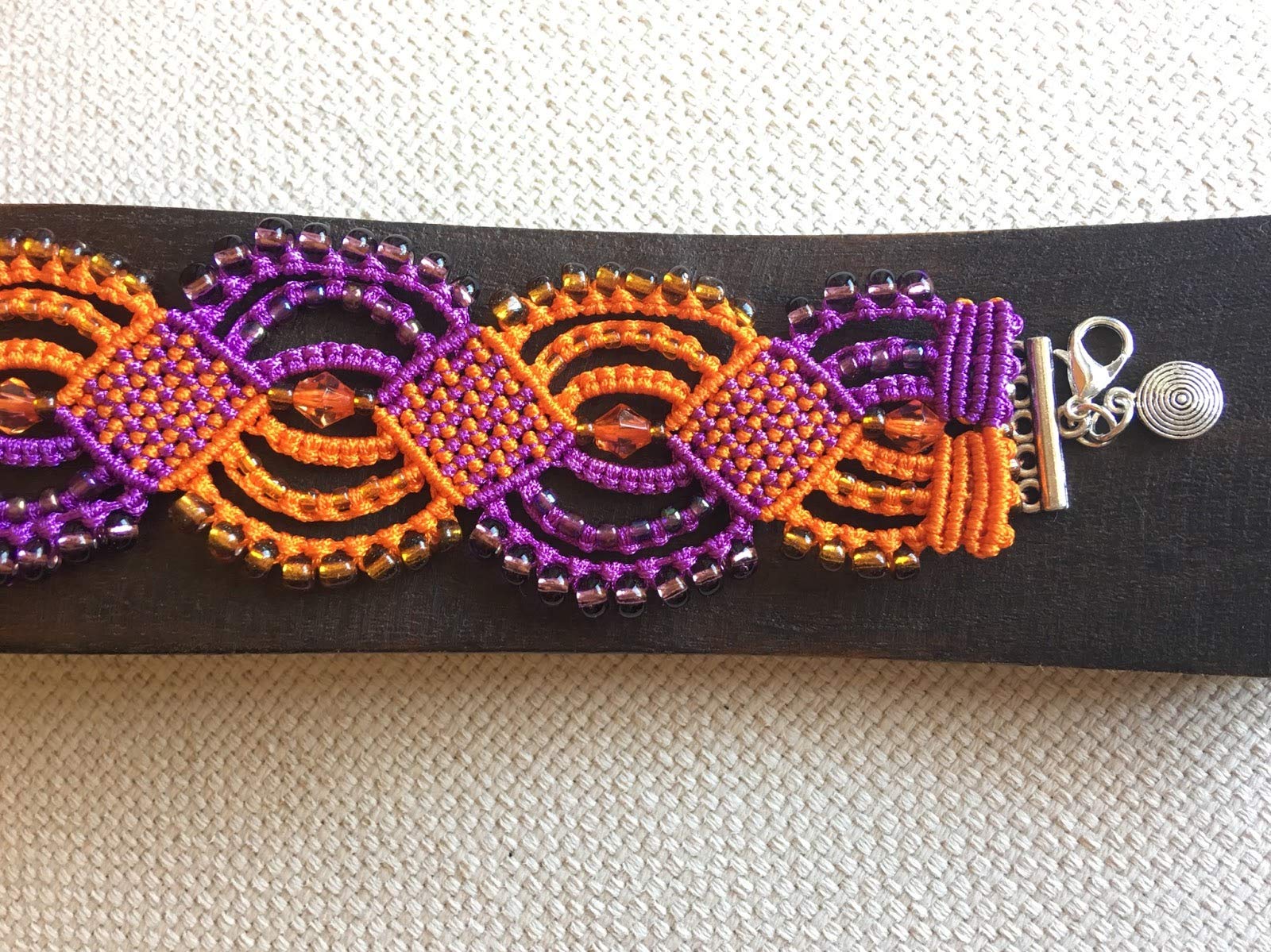Pulsera macrame morada y naranja hecha a mano con rocallas a juego Cierre y colgante. Mide aproximadamente 17 cm. de largo y 3,5 cm. de ancho