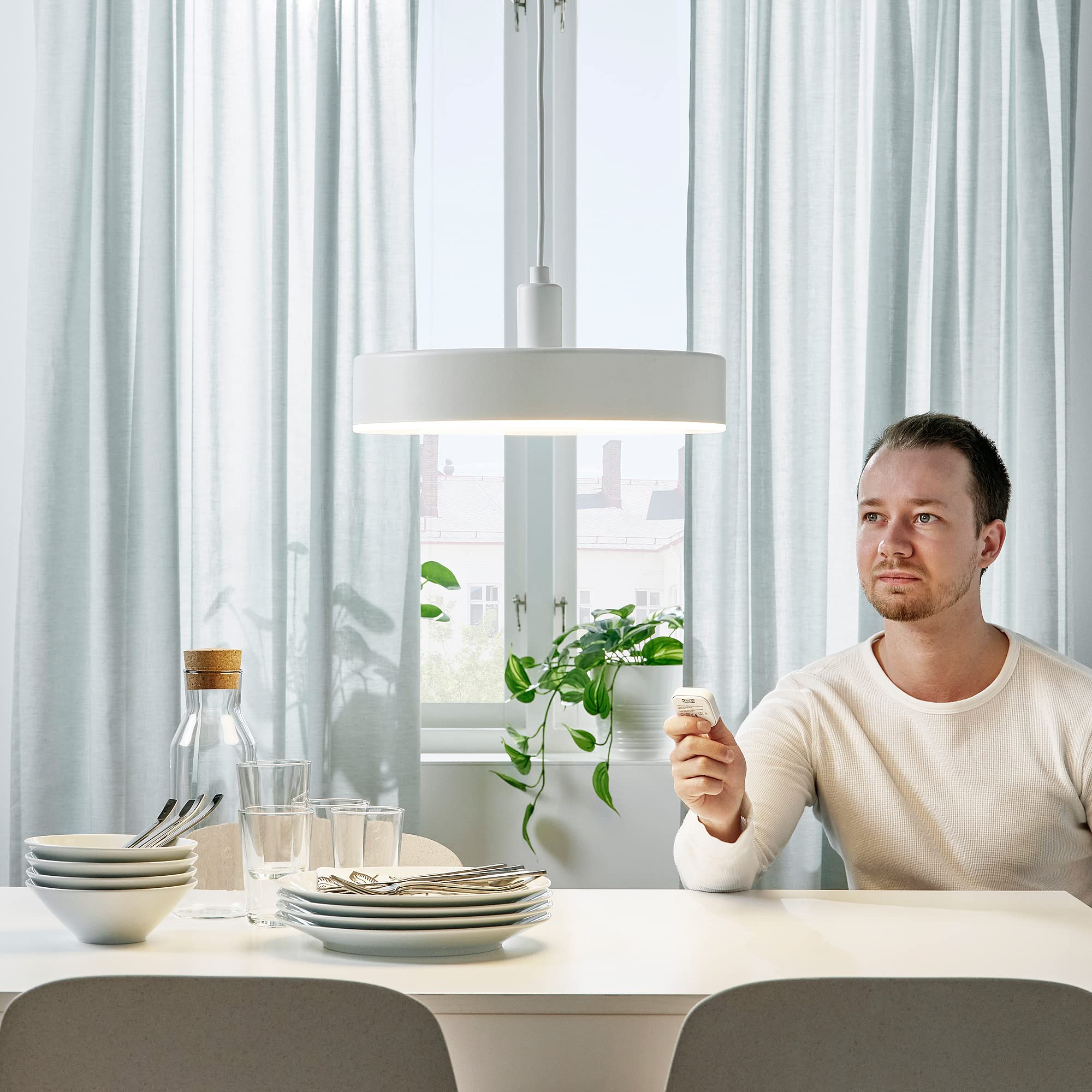 Man using a wireless dimmer to control the NYMÅNE LED Pendant Lamp