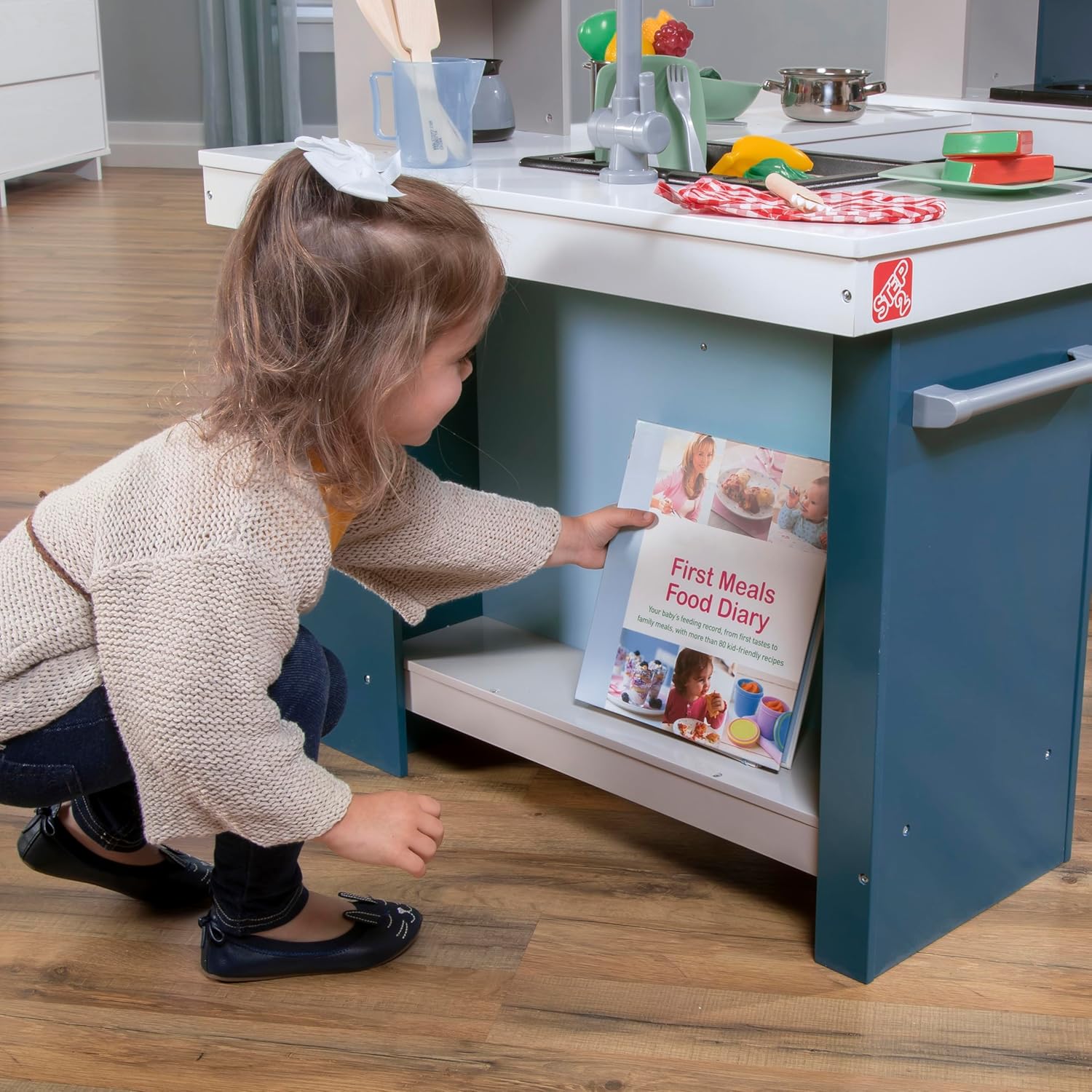 Child organizing play food in the storage shelves of the Step2 Grand Walk-In Wooden Kids Kitchen Playset.
