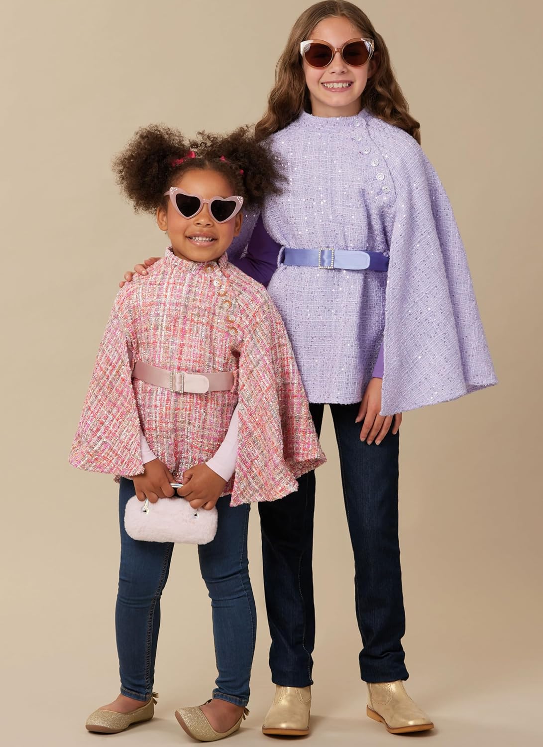 Young girl wearing a pink tweed cape with a stand collar and a light pink belt, smiling at the camera.