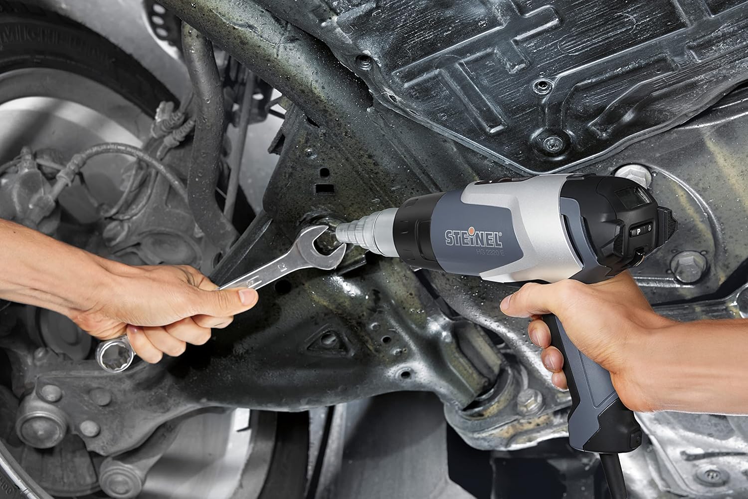 Person using Steinel HG 2320 E heat gun to loosen a bolt on a vehicle's undercarriage.