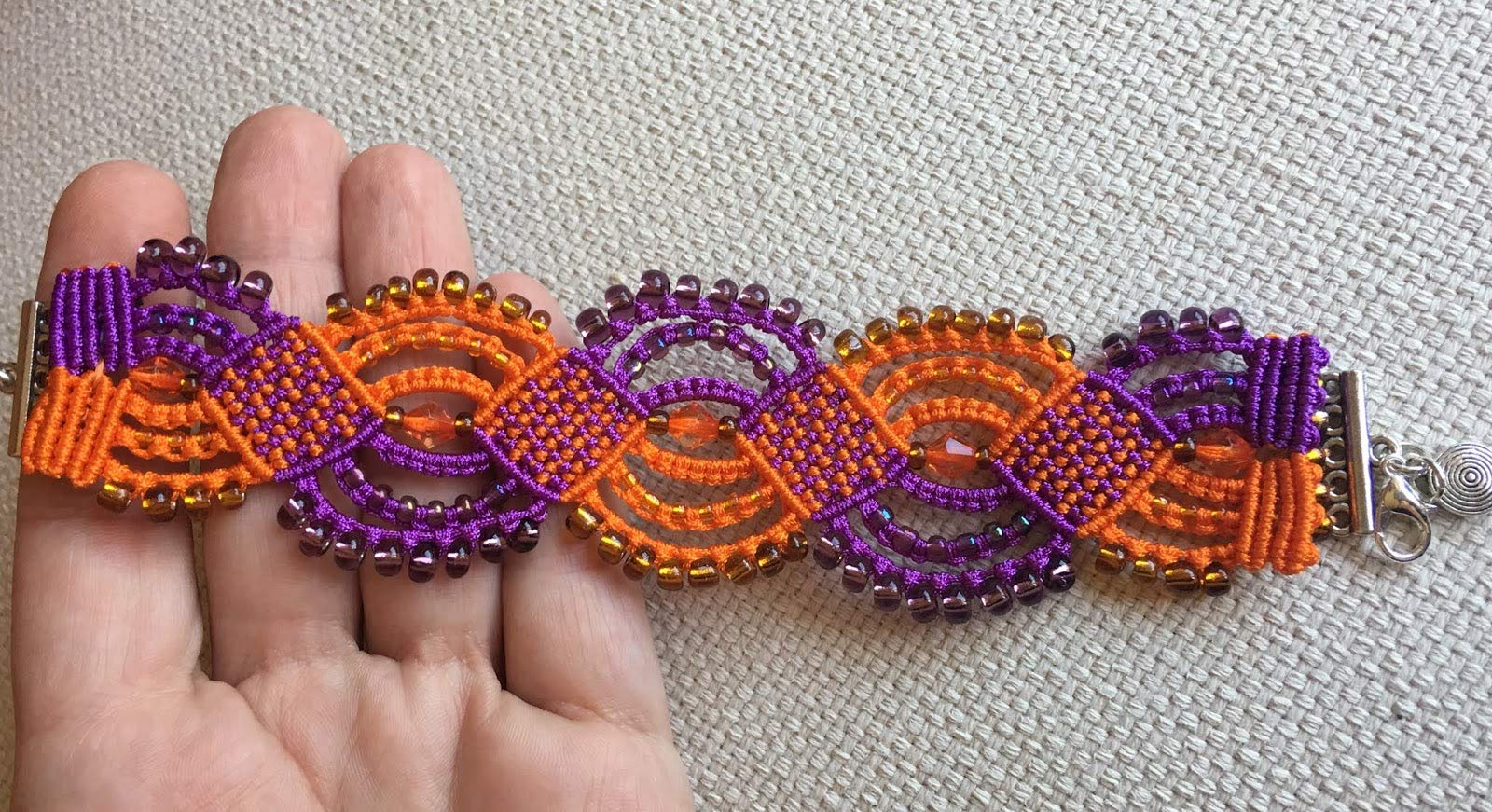 Pulsera macrame morada y naranja hecha a mano con rocallas a juego Cierre y colgante. Mide aproximadamente 17 cm. de largo y 3,5 cm. de ancho