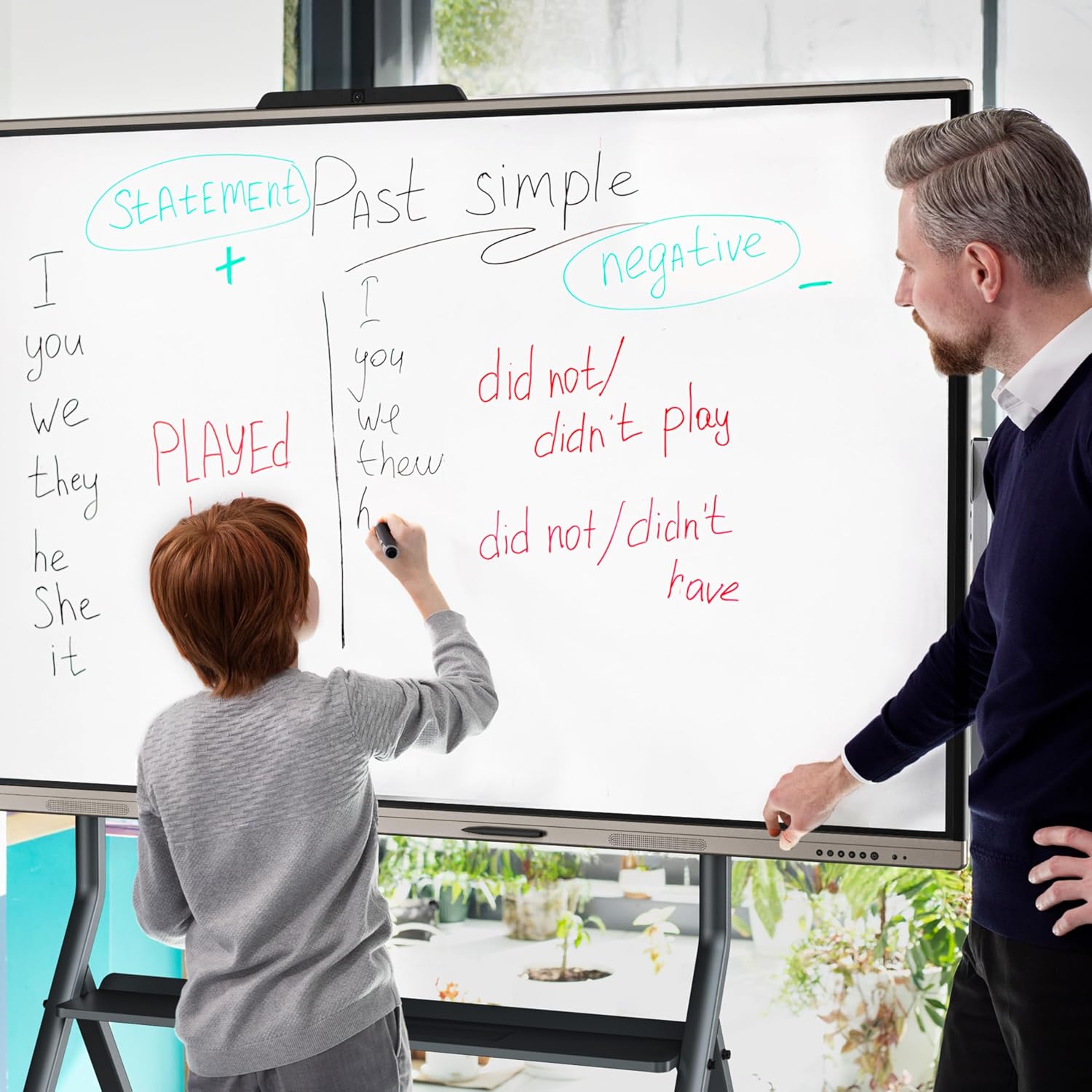 A child writing on the Faytech interactive whiteboard with a stylus, while an adult observes. The whiteboard displays English grammar lessons.