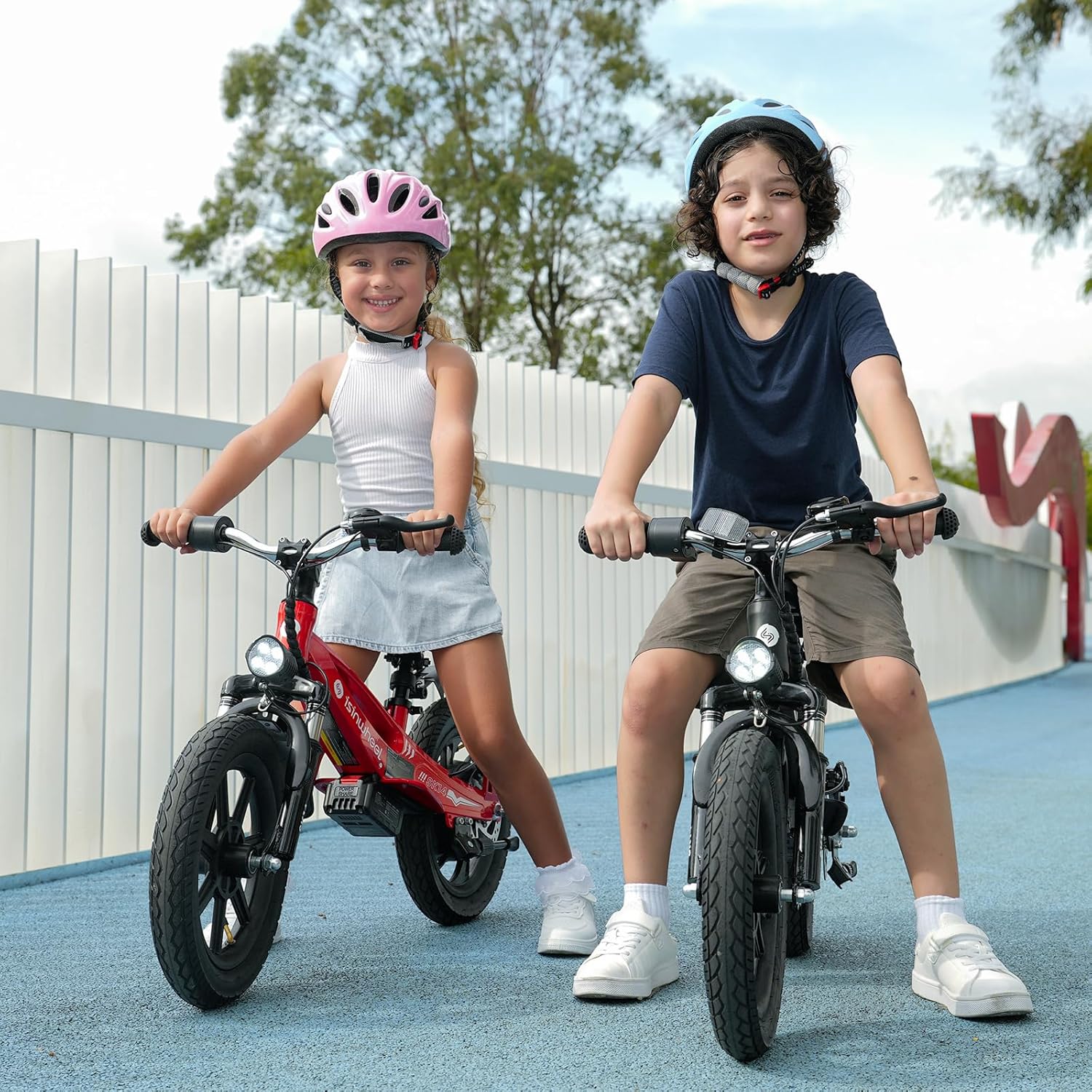 Two children, a girl on a red isinwheel SK14 and a boy on a black isinwheel SK14, standing side-by-side on a paved area.