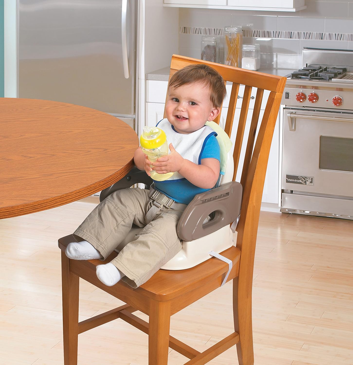 Happy baby sitting in the booster seat at a dining table, holding a bottle