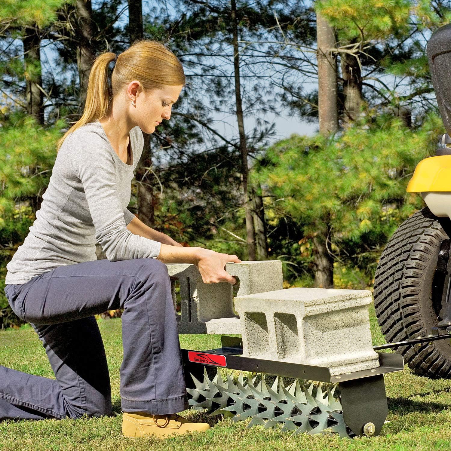 Woman placing concrete blocks onto the weight tray of the Brinly Spike Aerator