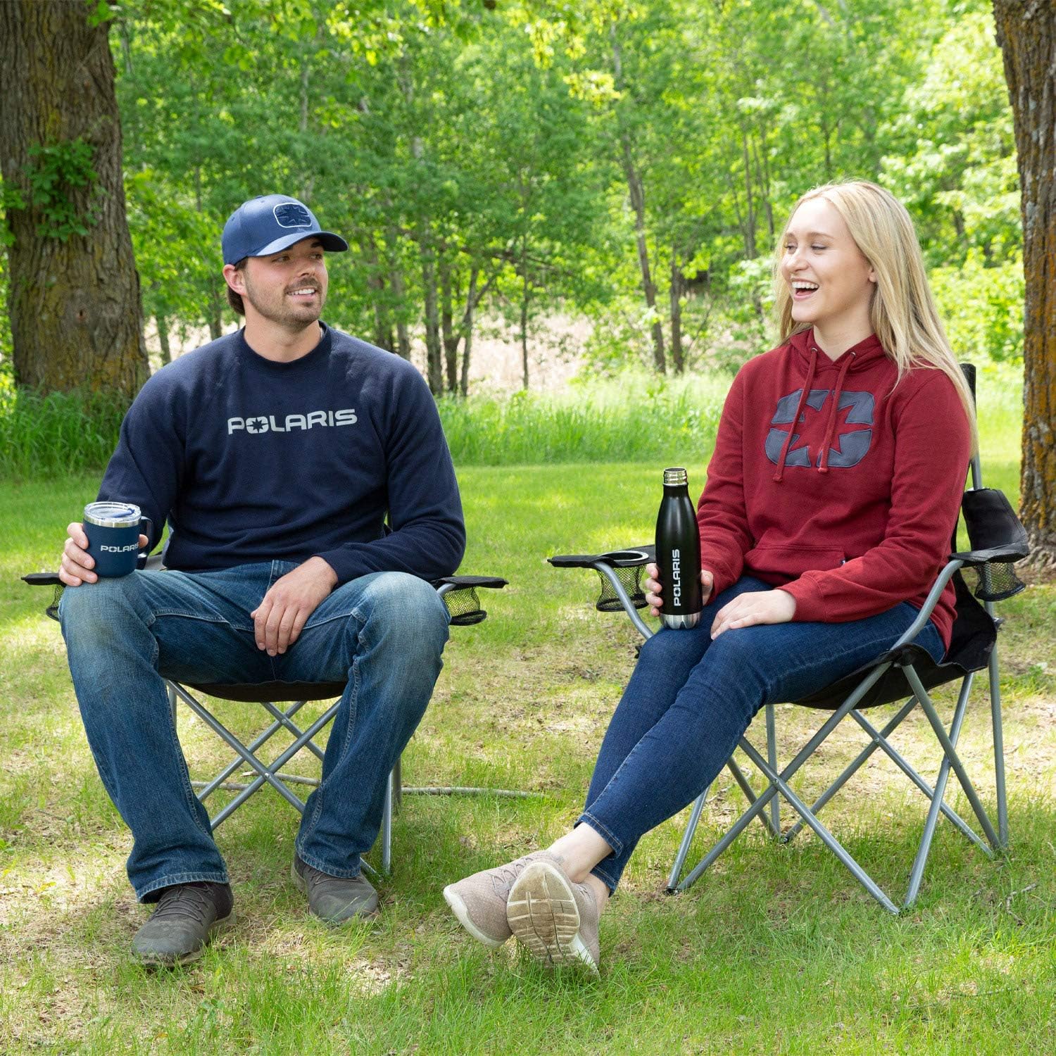 Two people sitting in camping chairs outdoors, one holding a Polaris mug.
