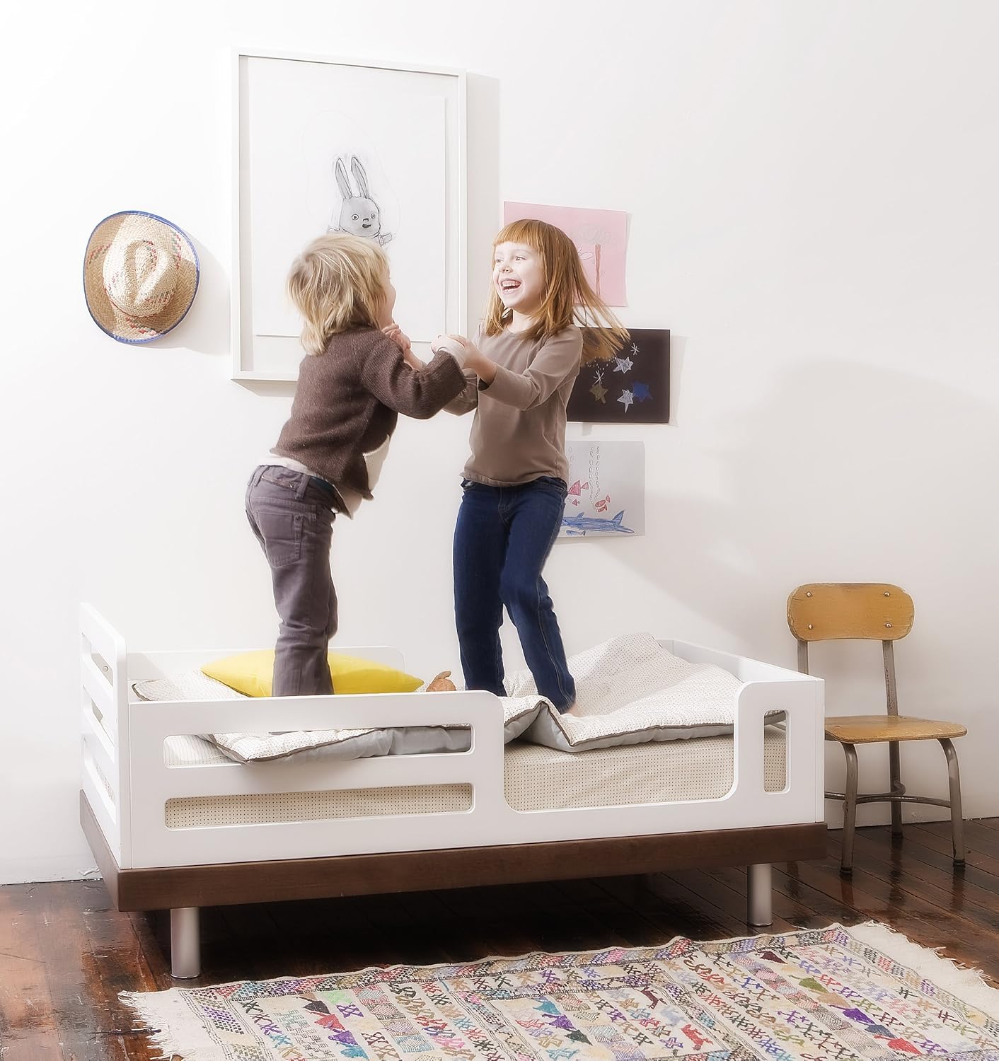 Two children jumping on the Oeuf Classic Toddler Bed, demonstrating its sturdy construction.