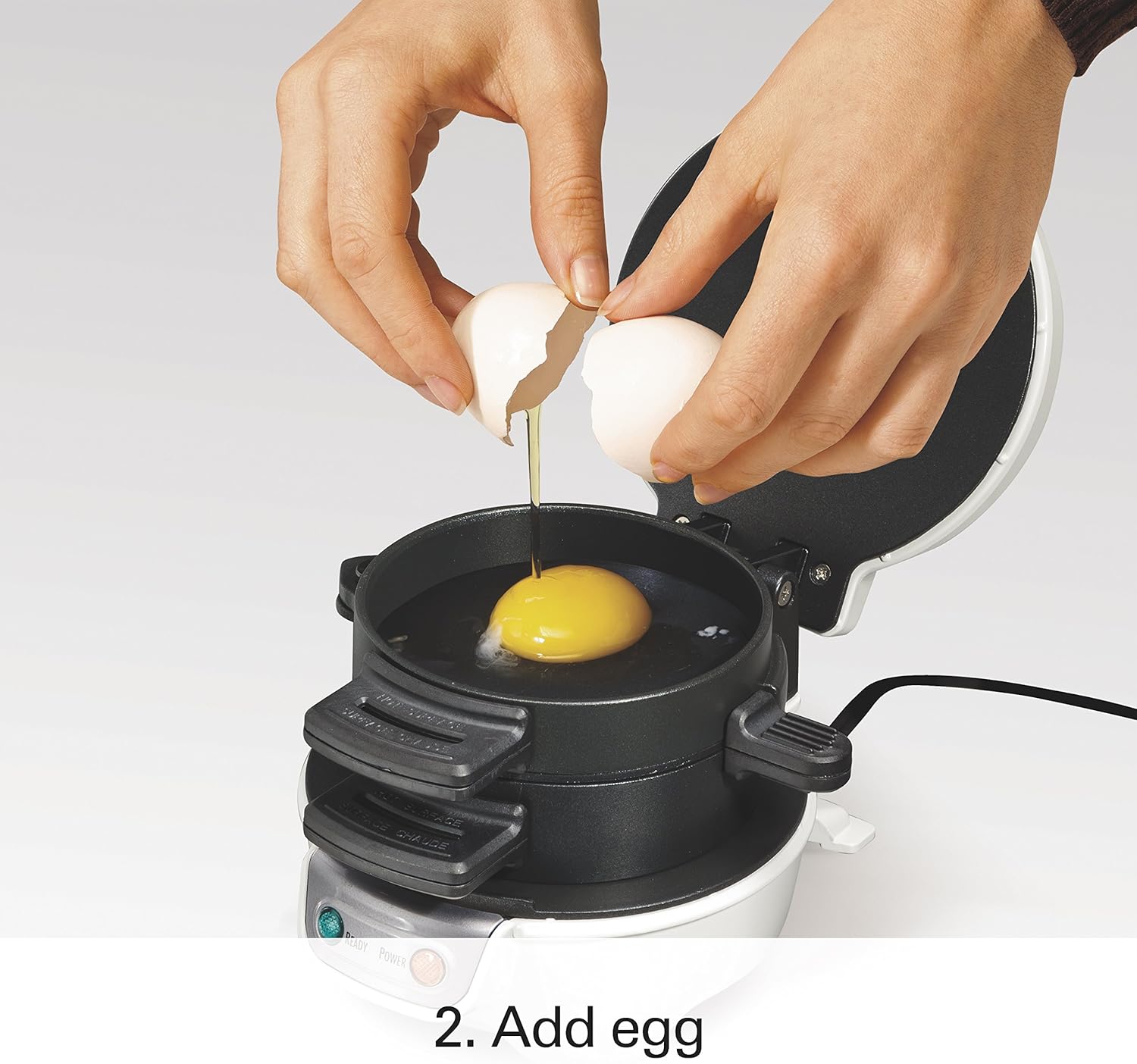 A hand cracking an egg directly into the middle cooking ring of the sandwich maker.