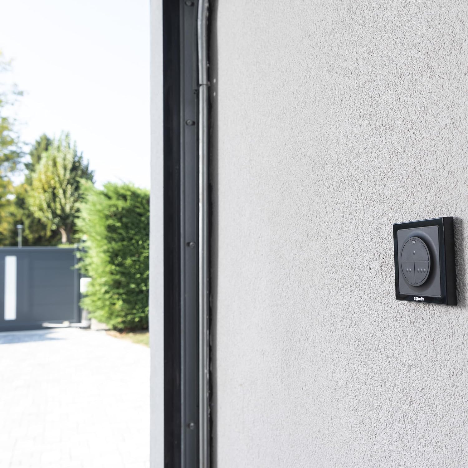 Somfy 1870781 RTS 3-Button Wireless Wall Control mounted on an exterior wall next to a garage and gate
