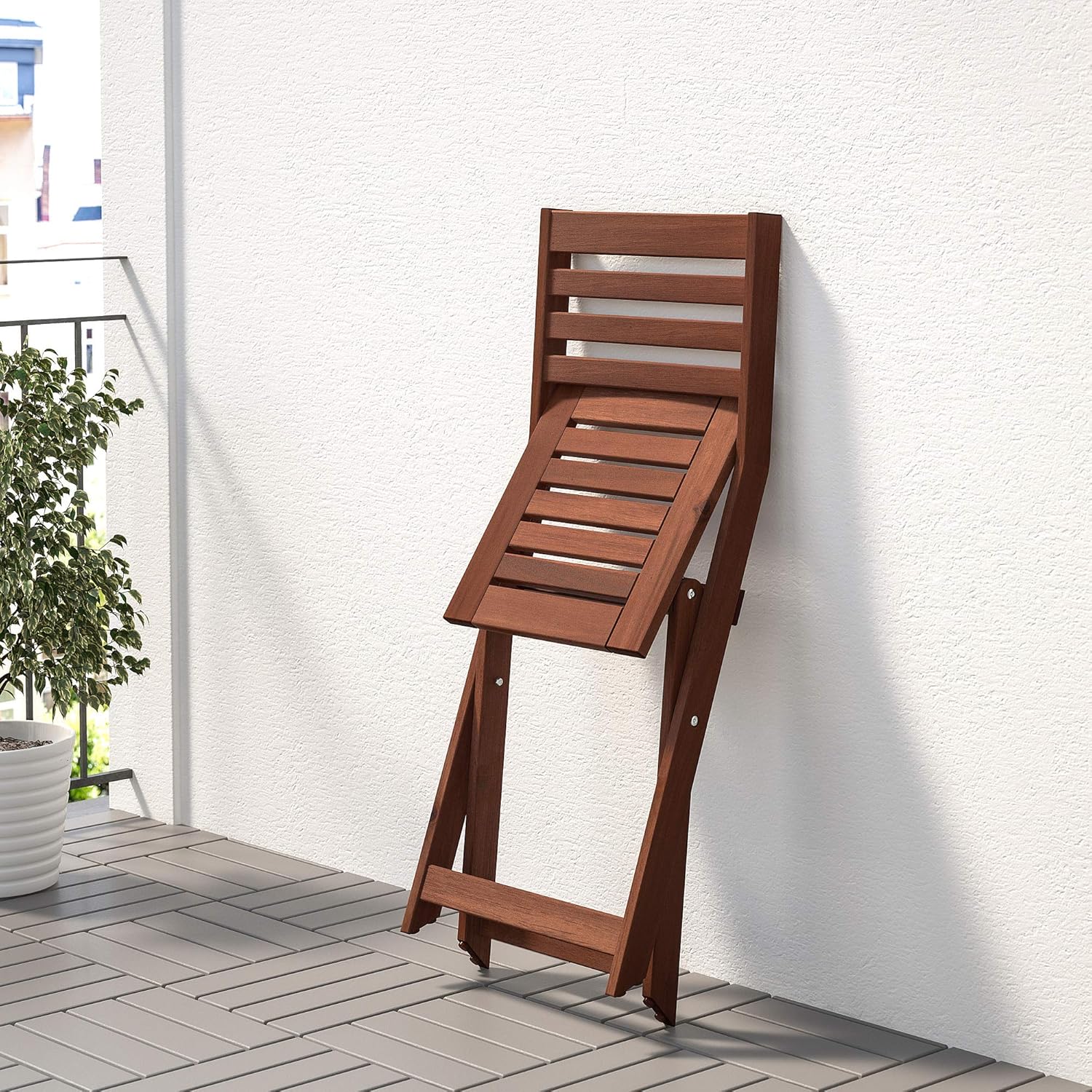 IKEA ÄPPLARÖ outdoor foldable chair folded and leaning against a white wall on a patio.
