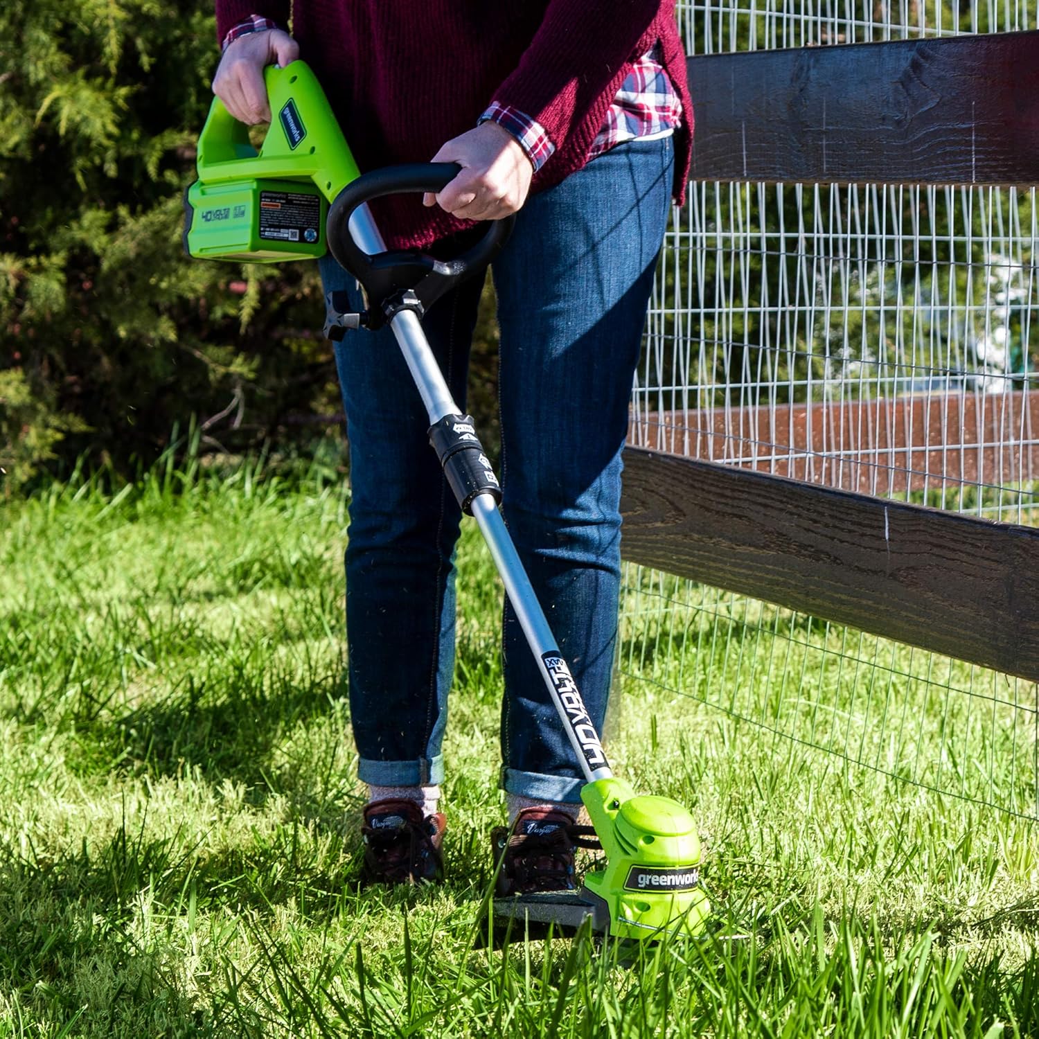 User operating the Greenworks string trimmer near a wooden fence