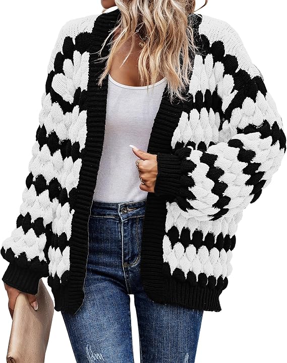 Open-front chunky knit cardigan in bold black and white color-block pattern with voluminous lantern sleeves and ribbed cuffs, worn over a white top and blue jeans. Front view.