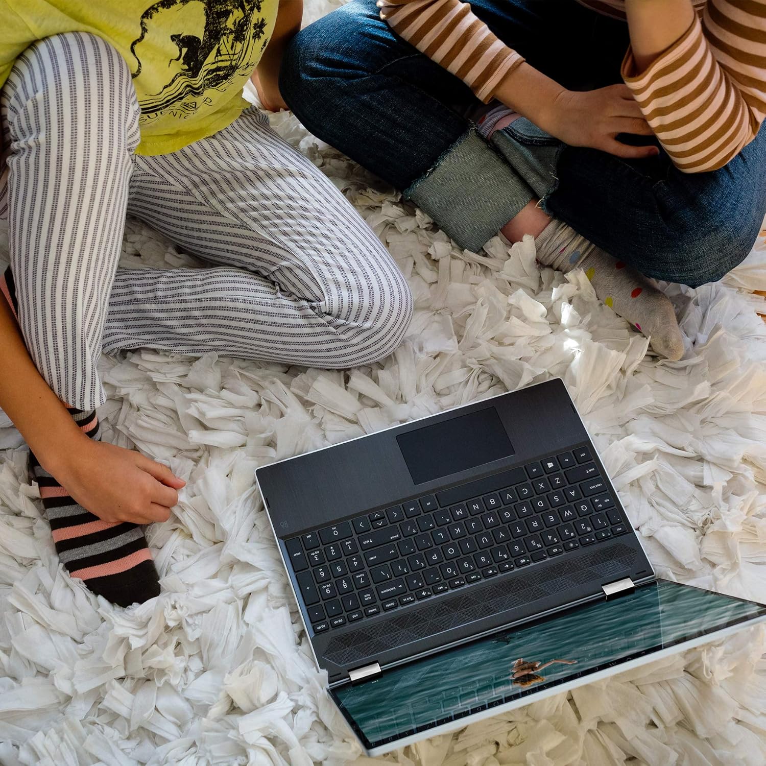 HP Pavilion x360 in tent mode, used by two people on a rug.