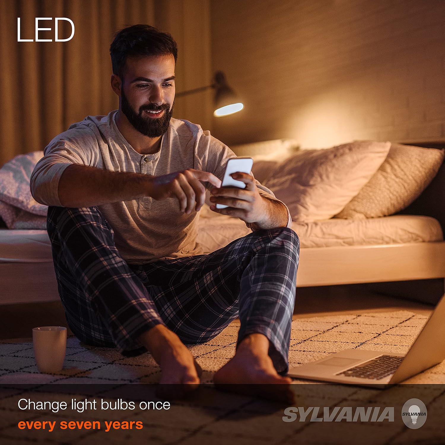 SYLVANIA LED лампасынын жарыгы менен уктоочу бөлмөдө смартфон колдонуп жаткан адам