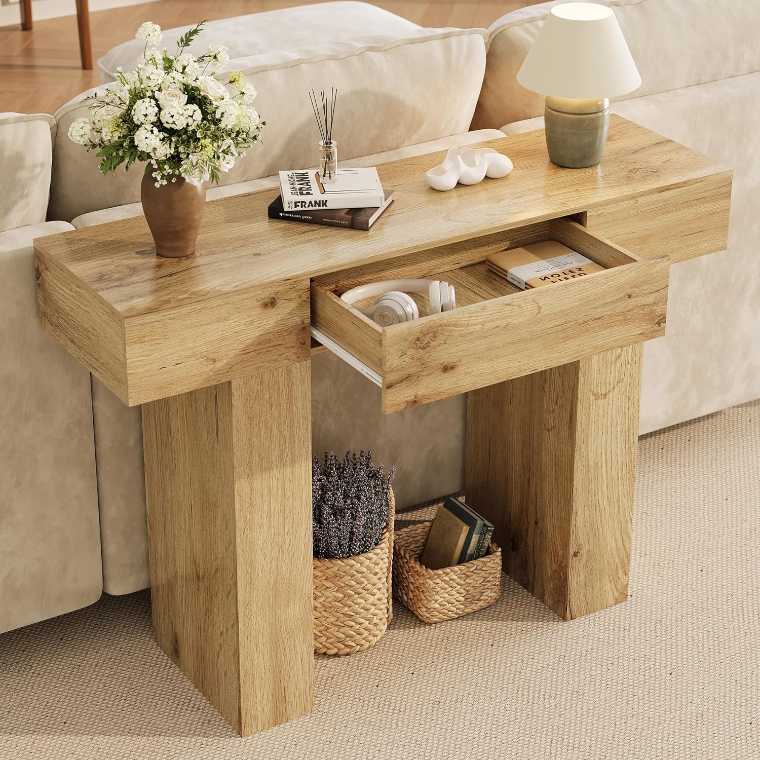 The Garvee console table placed behind a sofa, showcasing its use as a sofa table with decorative items and an open drawer revealing stored headphones and books.