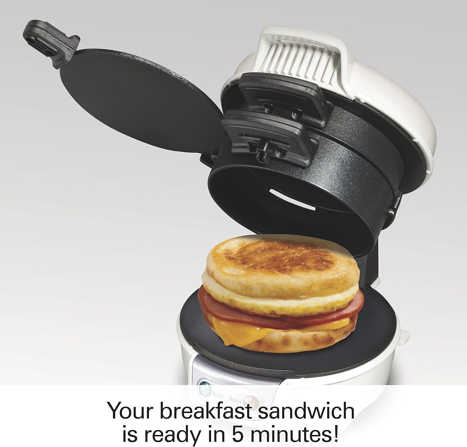 A hand sliding the egg plate out from the sandwich maker to combine the sandwich layers.