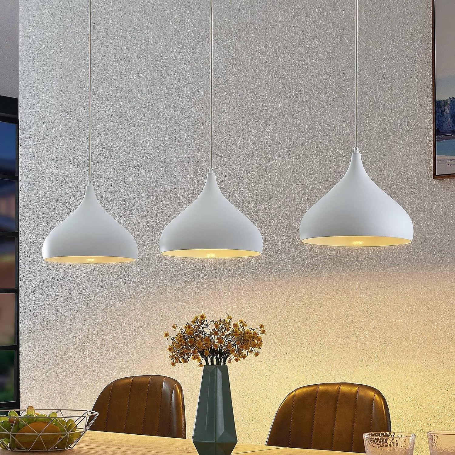 Lindby Elamira 3-light pendant lamp illuminated over a dining table with chairs and a vase, showcasing its modern design and downward light distribution.