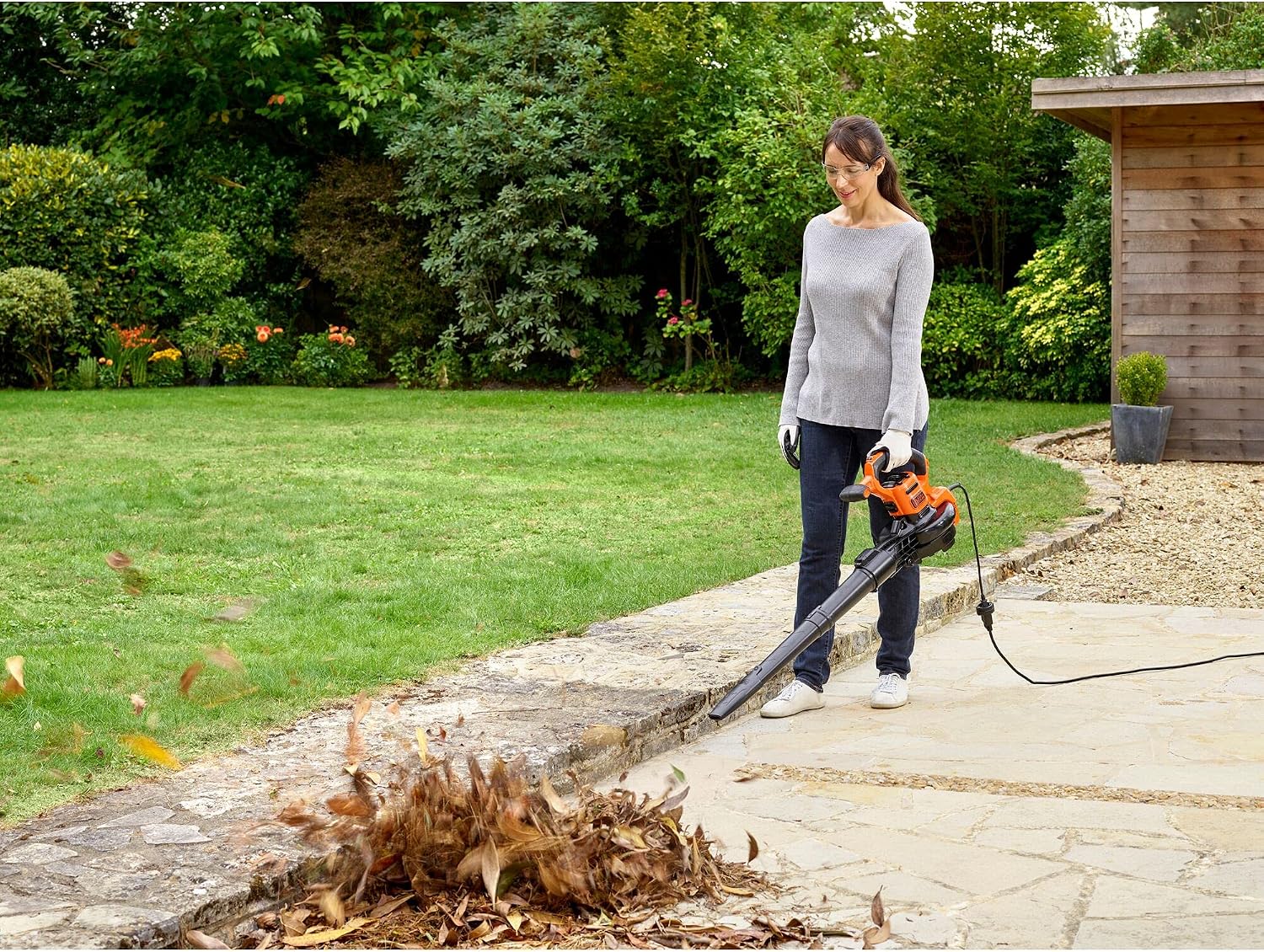 A person using the BLACK+DECKER BEBLV301 in blower mode to clear leaves from a lawn