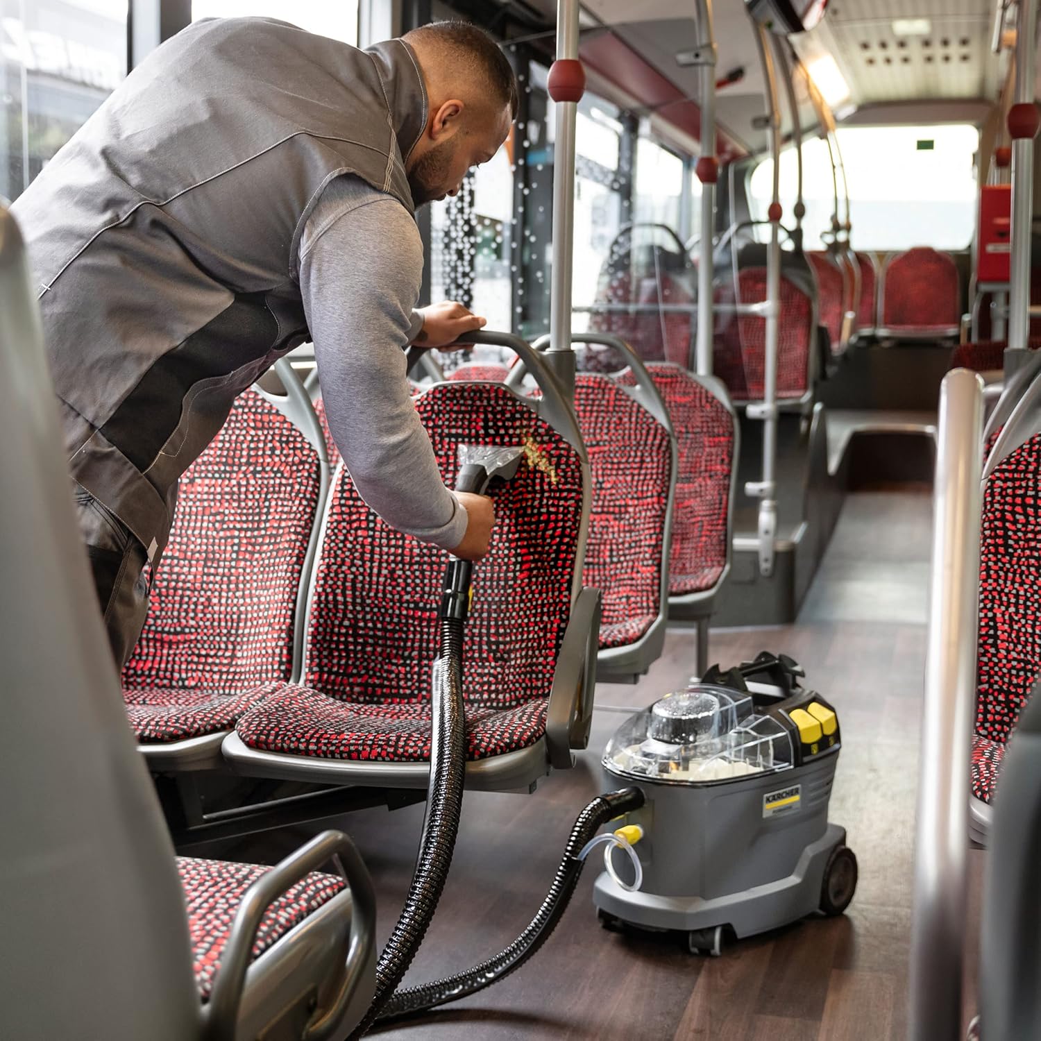 Man cleaning red and black patterned bus seats with the Kärcher Puzzi 8/1