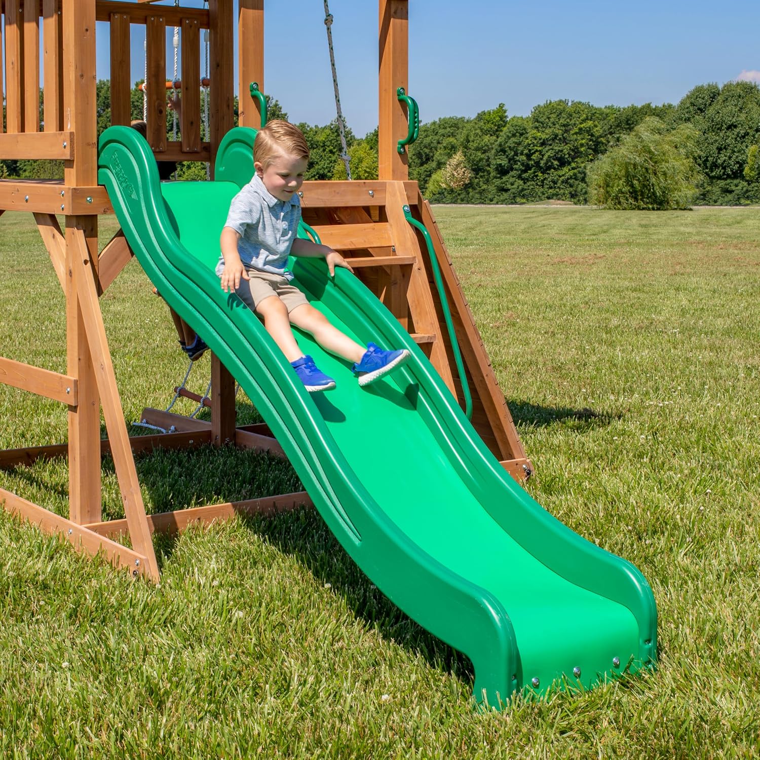A young boy sliding down the green wave slide of the playset.