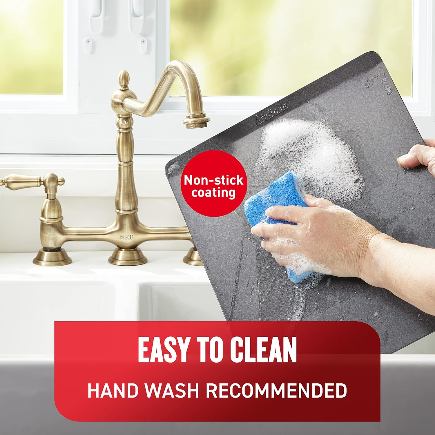A hand washing an AirBake cookie sheet with a sponge and soap, text 'EASY TO CLEAN HAND WASH RECOMMENDED'