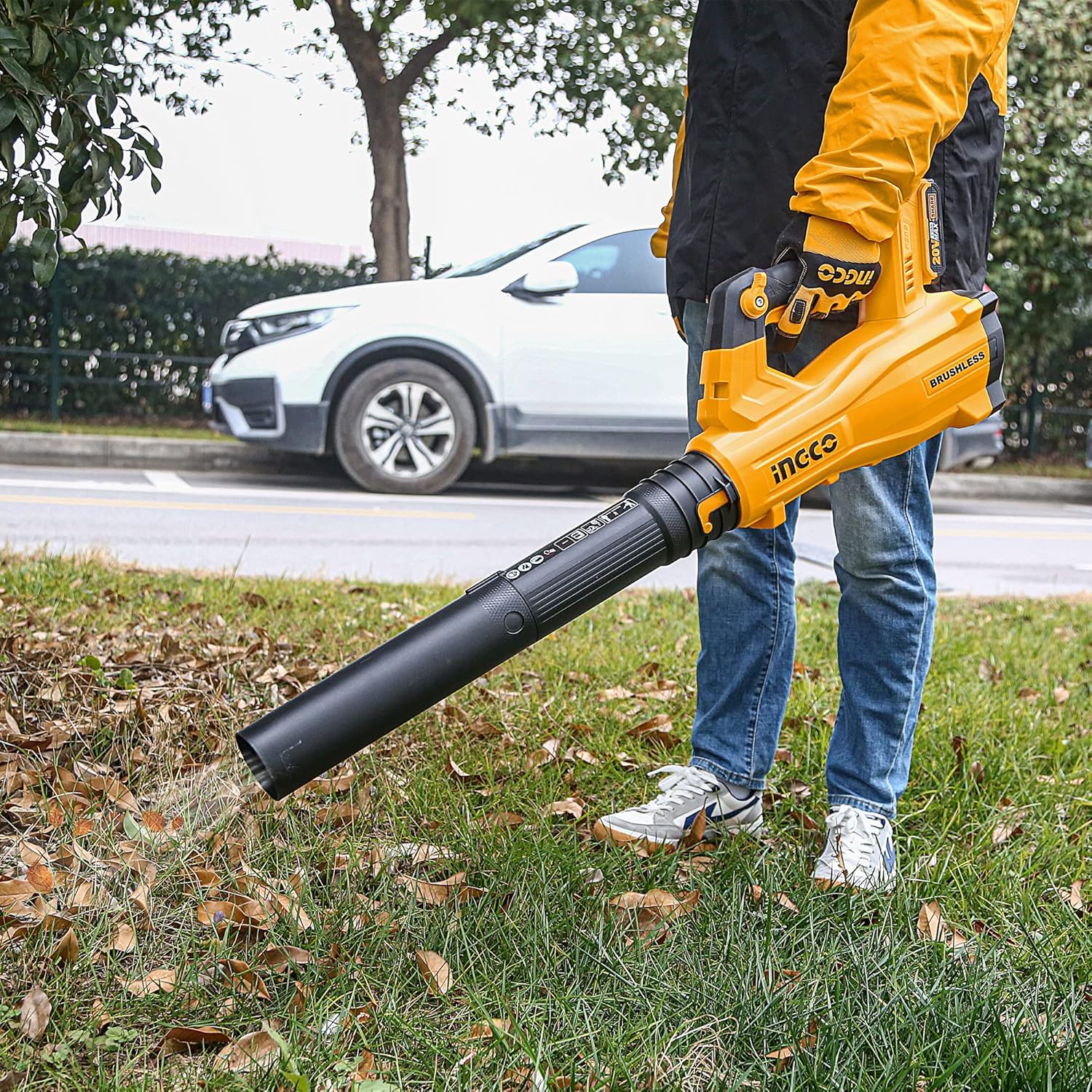 Person using INGCO leaf blower to clear leaves from a grassy area