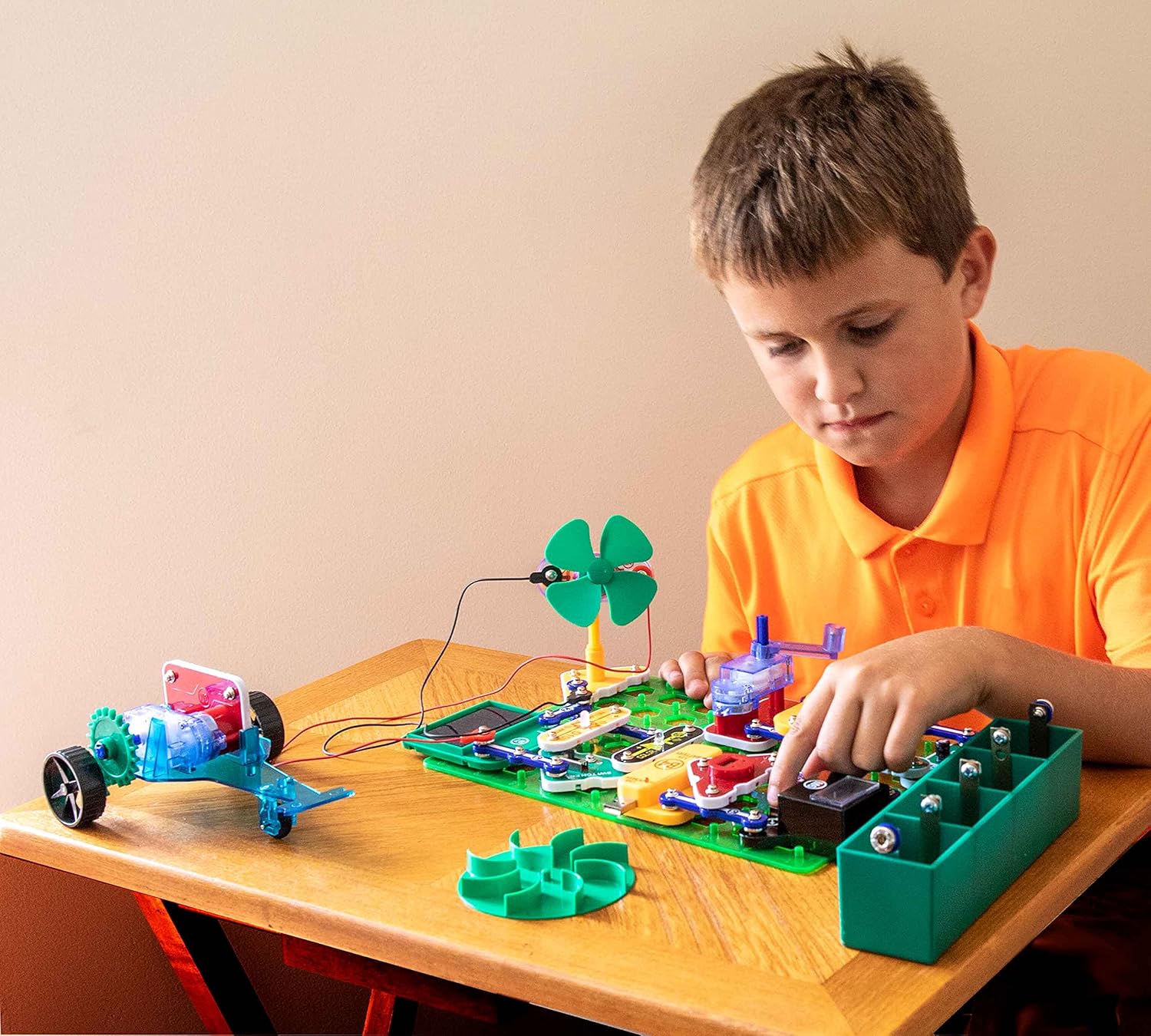 A child assembling a Snap Circuits project on a green base grid.