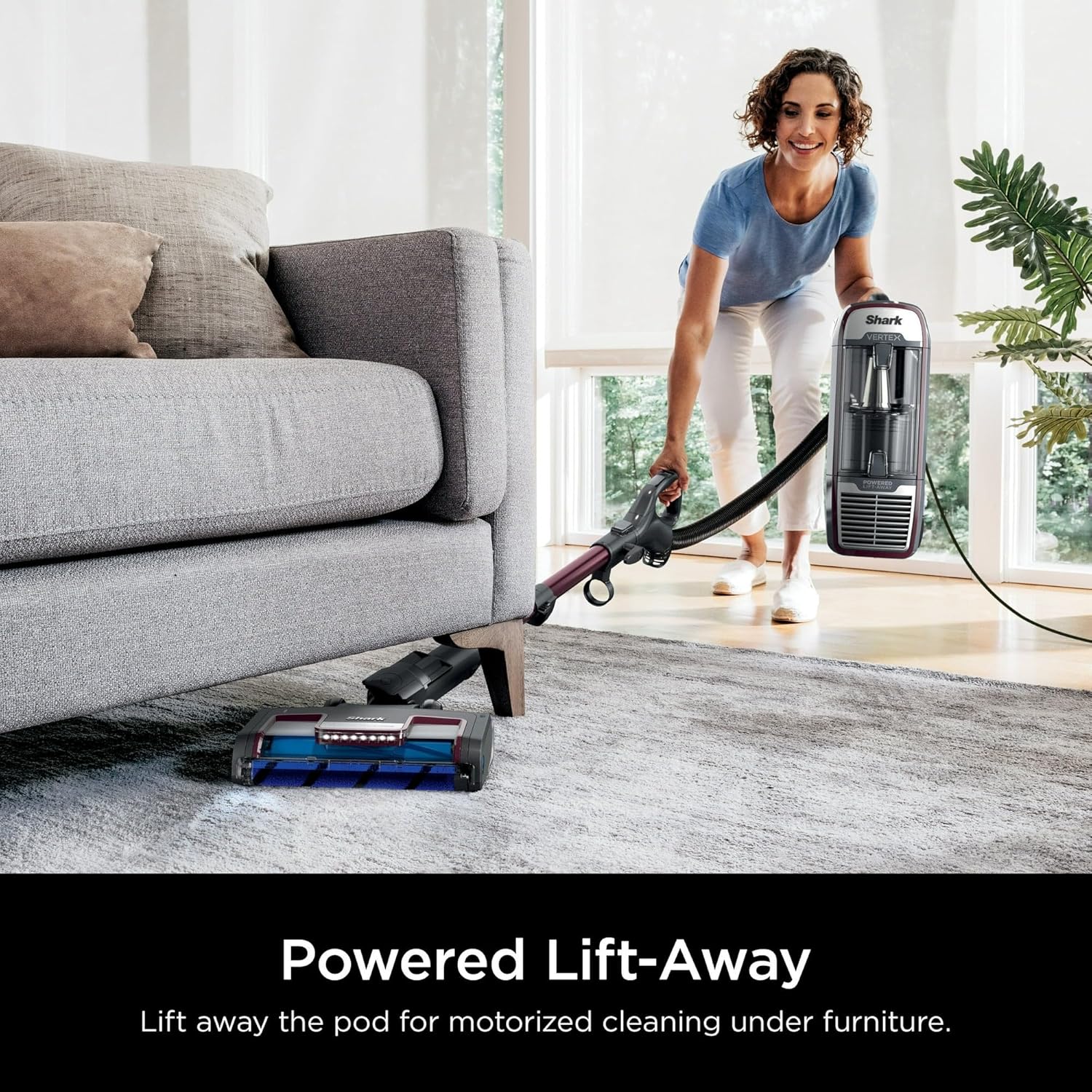 Woman using the Powered Lift-Away feature to clean under a sofa