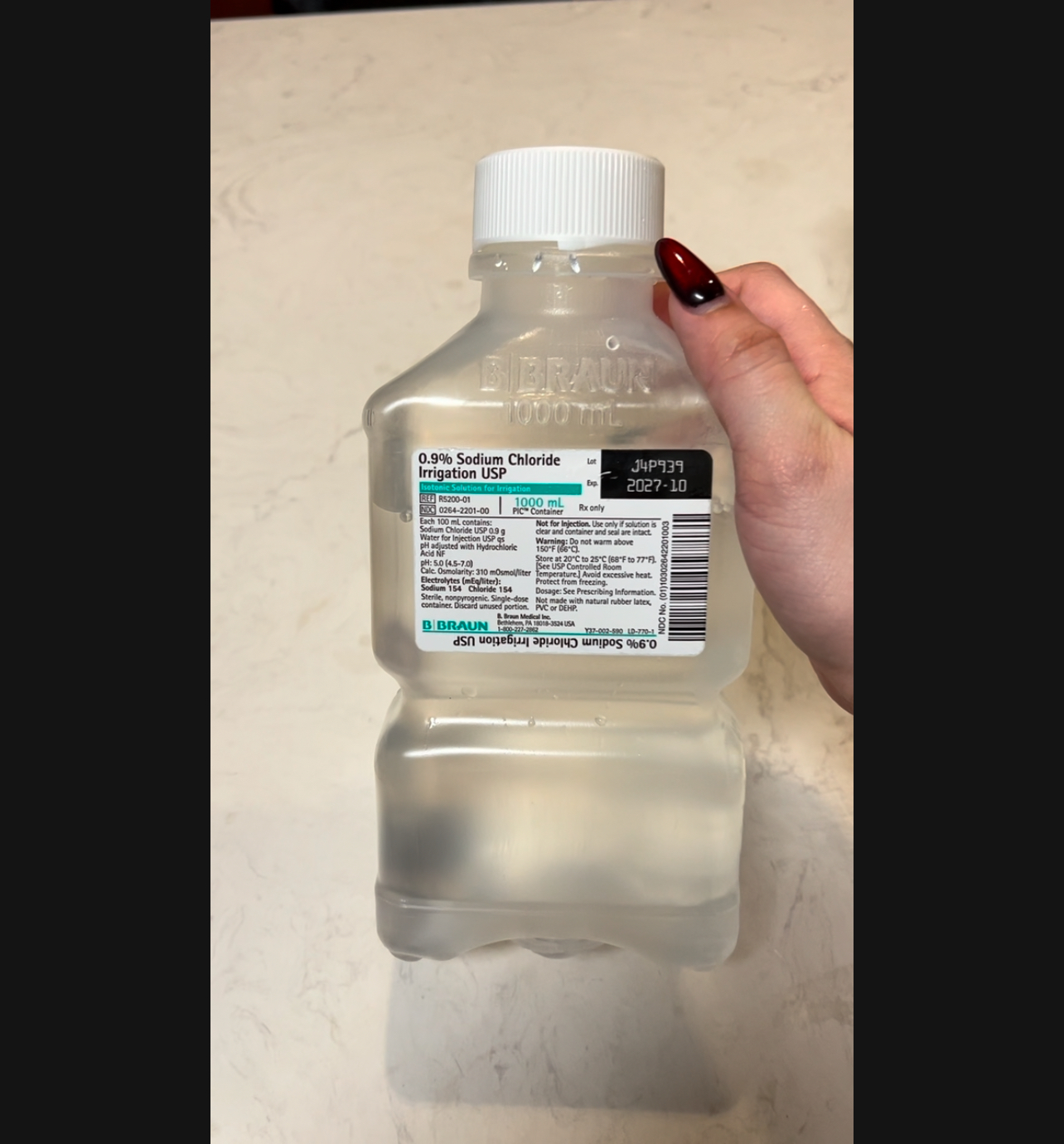 Hand holding a 1000ml bottle of Normal Saline, demonstrating its easy handling.