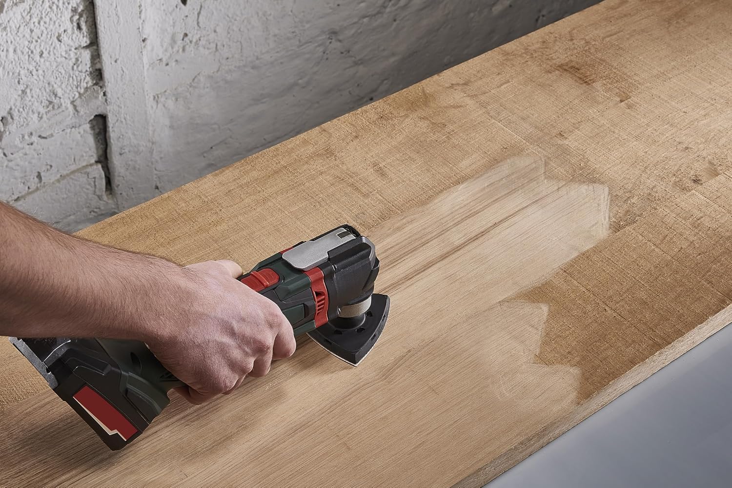A person using a red and black multi-sander with a Wolfcraft sanding sheet on a wooden surface.