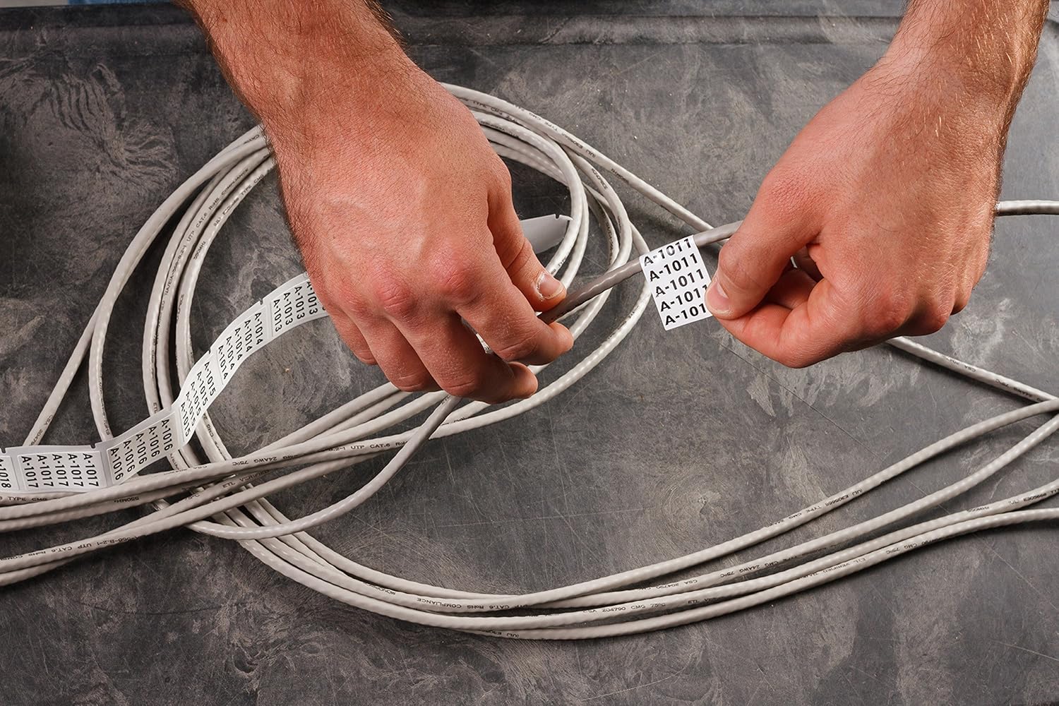 Hands applying self-laminating labels to network cables