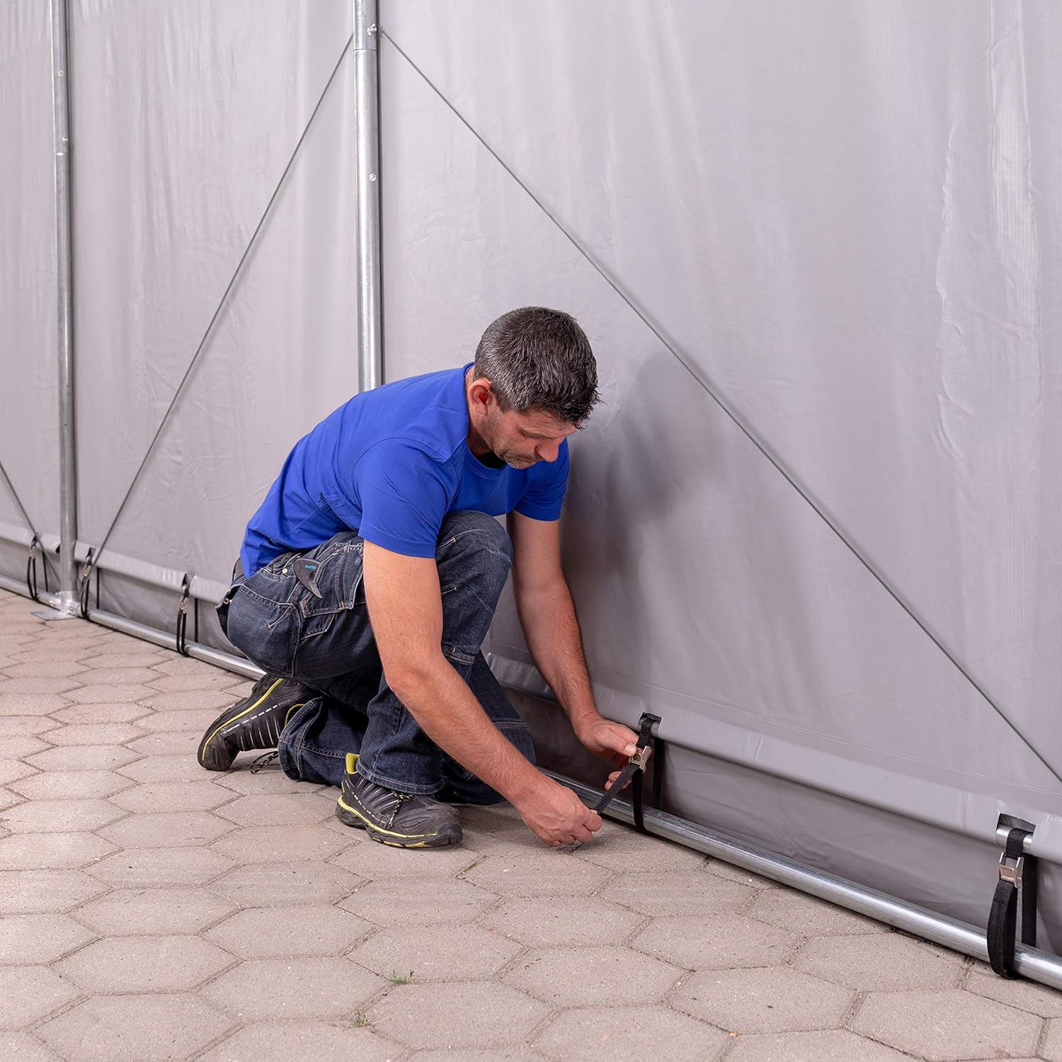 A person securing the tent tarp to the ground using a strap and anchor point.